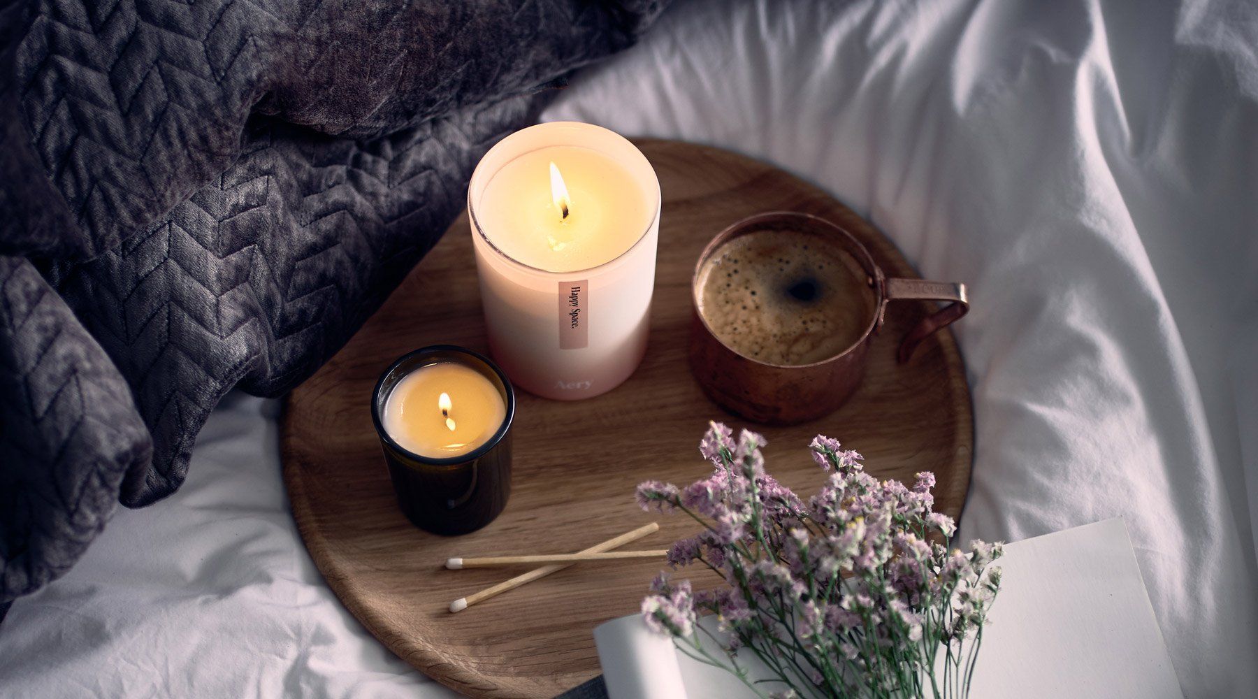 aery candes on wooden tray on top of a blanket in bed with a coffee and a book