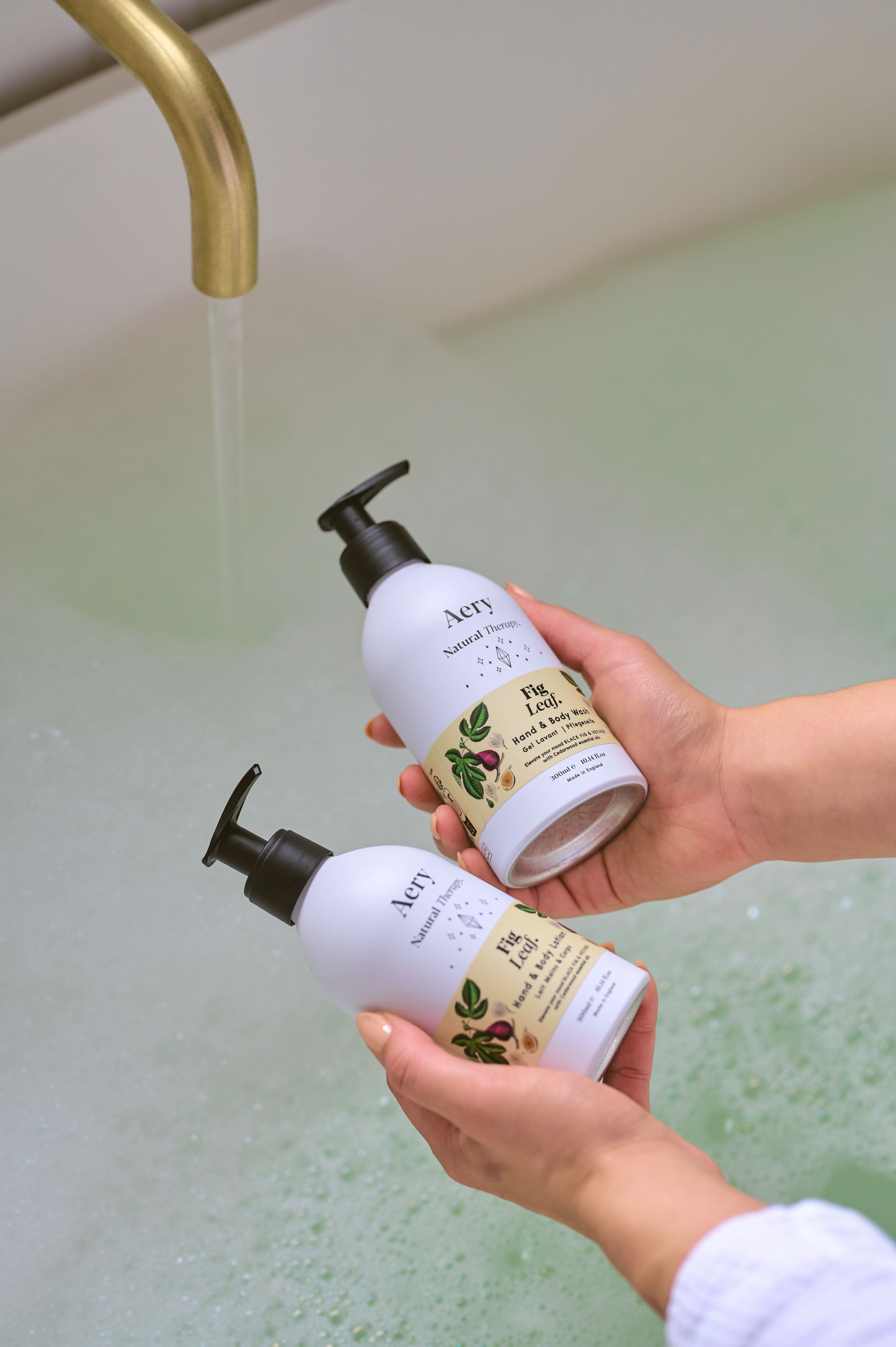 Cream Fig Leaf hand and body wash and lotion duo by Aery displayed in hands over bubble bath