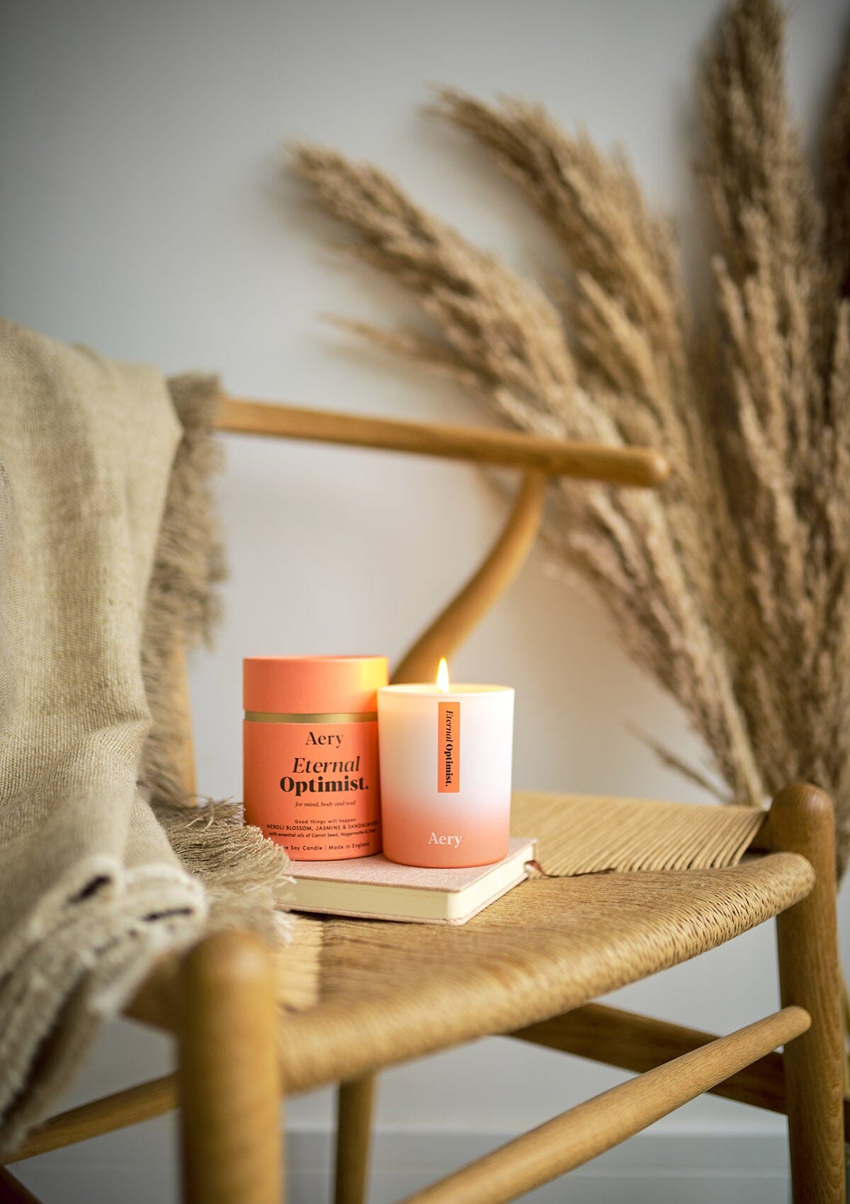 Orange Eternal Optimist candle displayed next to product packaging by Aery placed on wicker chair 