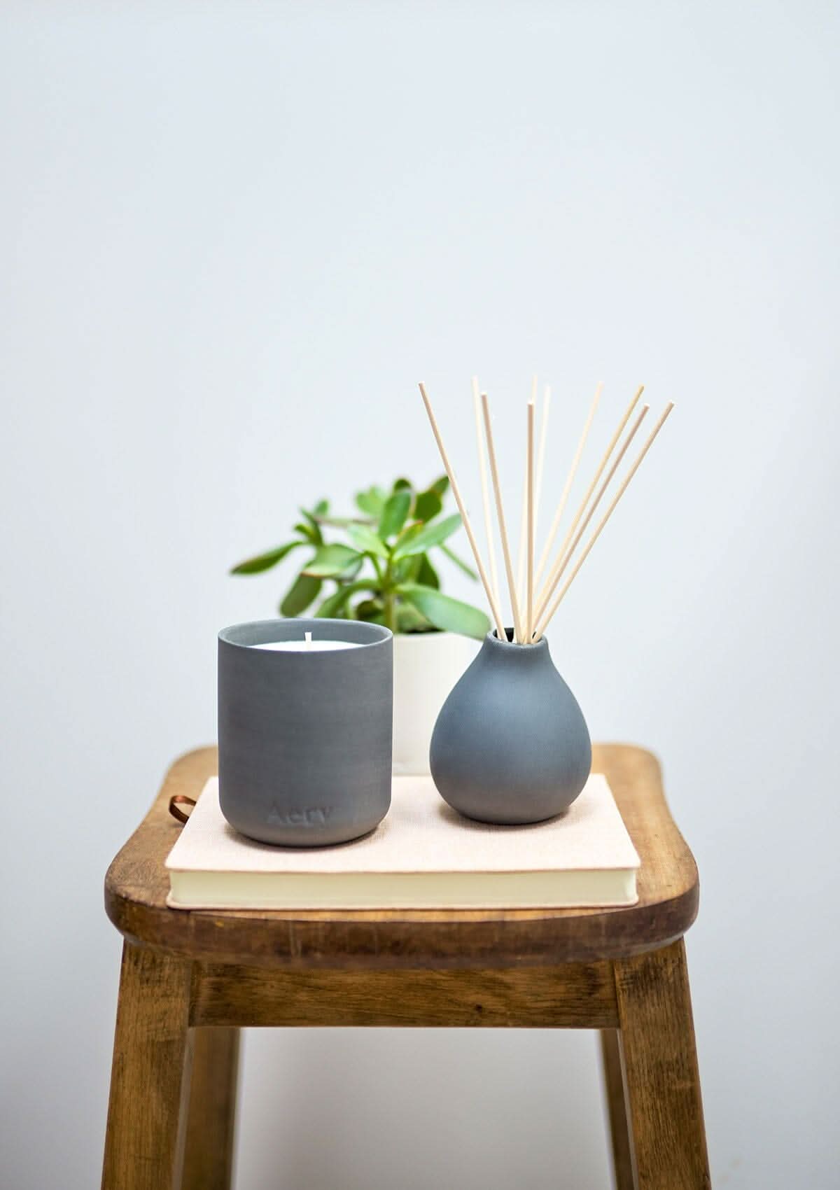 Black Indian Sandalwood Candle by Aery displayed next to Indian Sandalwood Diffuser placed on book and wooden Stool