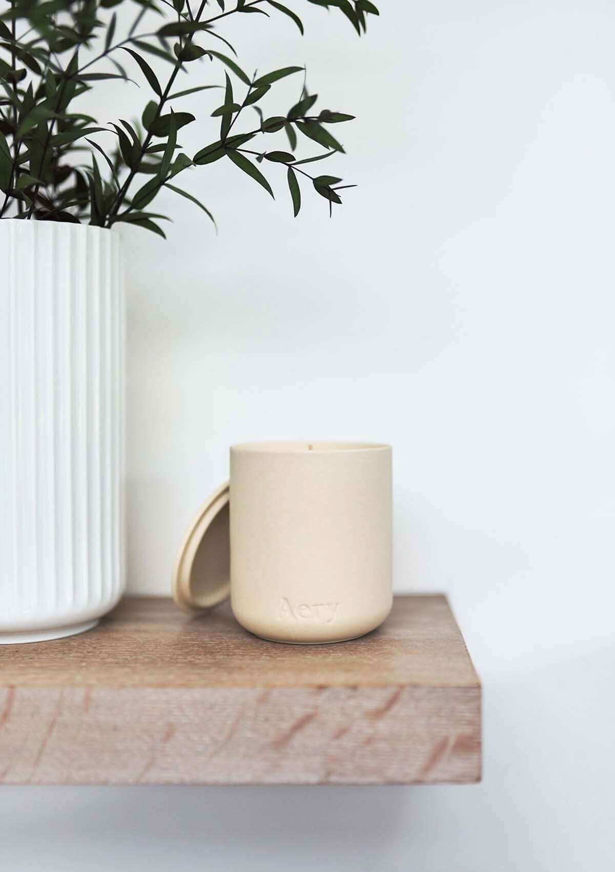 Cream Himalayan Cedarleaf candle by Aery displayed next to potted plant sat on a wooden shelf