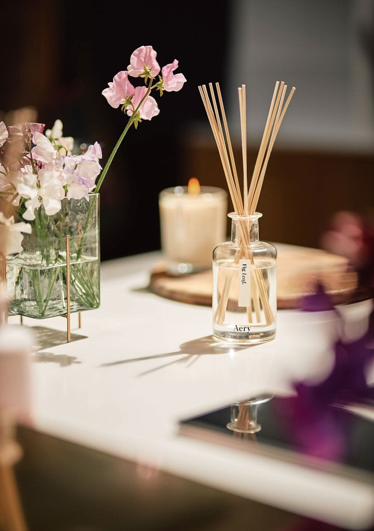 Cream Fig Leaf reed diffuser by aery displayed next to vase of white flowers on kitchen worktop