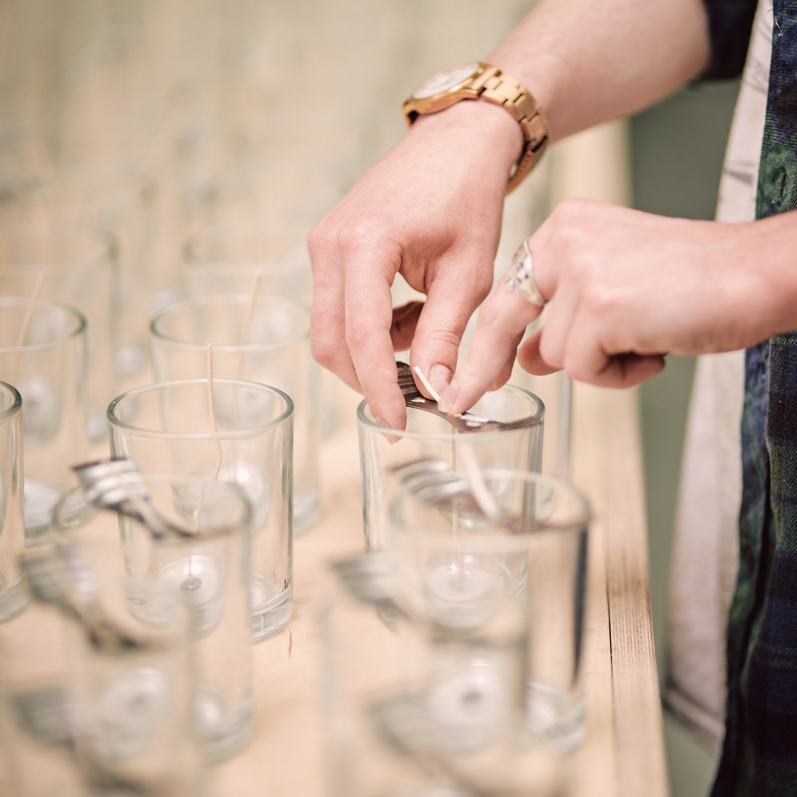 persons hand sticking wicks in candle vessels ready for candle making