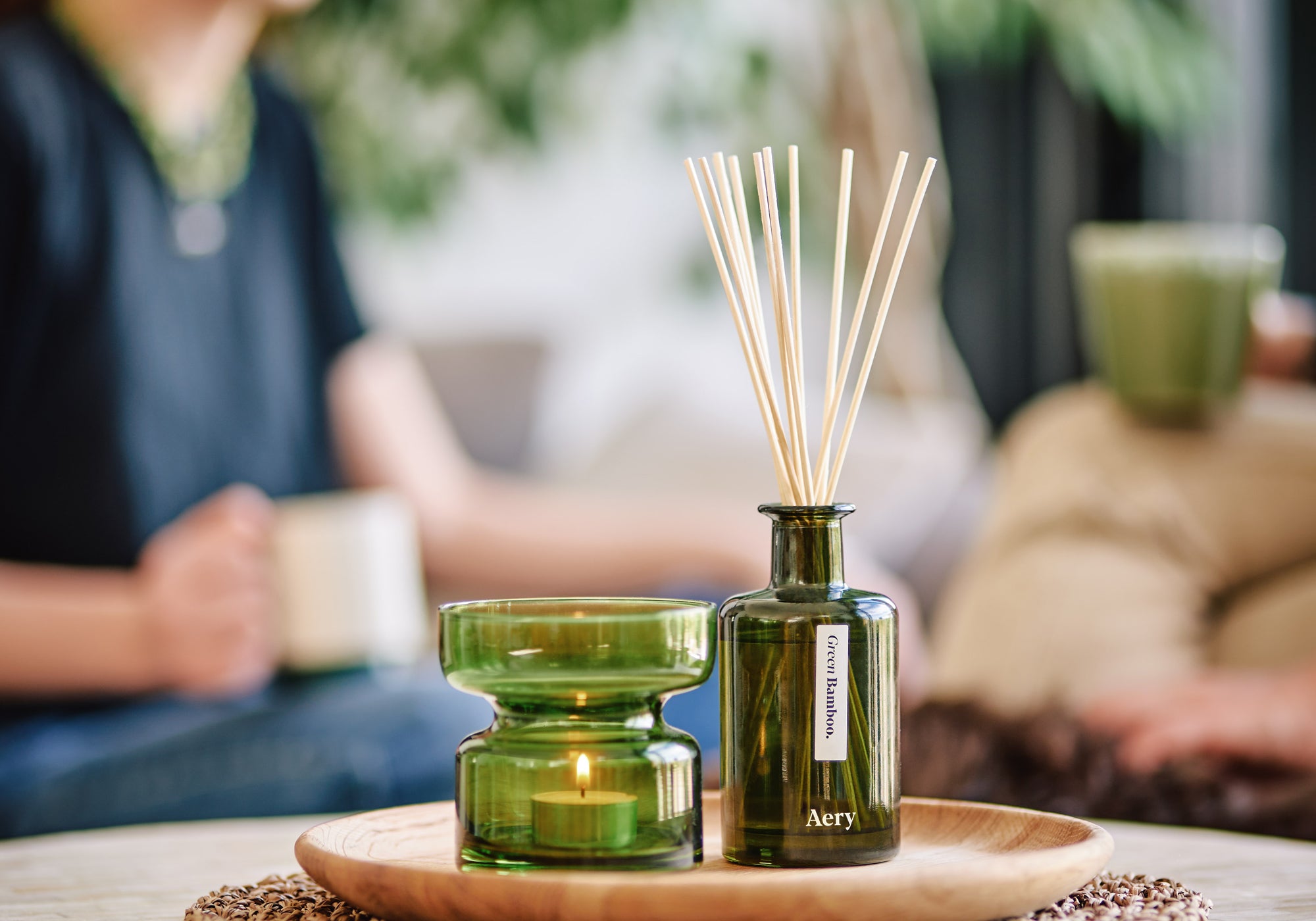 green bamboo aery living green glass reed diffuser displayed on coffee table next to decorative green tea light holder with two people in the background
