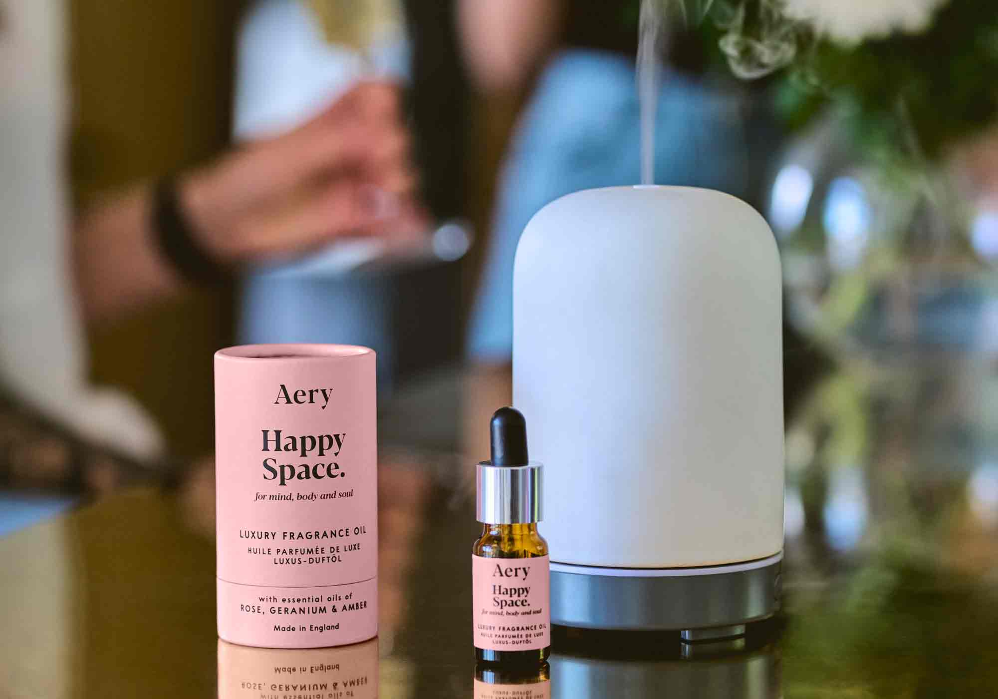 happy space pink aery living fragrance oil displayed next to product packaging and air diffuser on a brass counter top