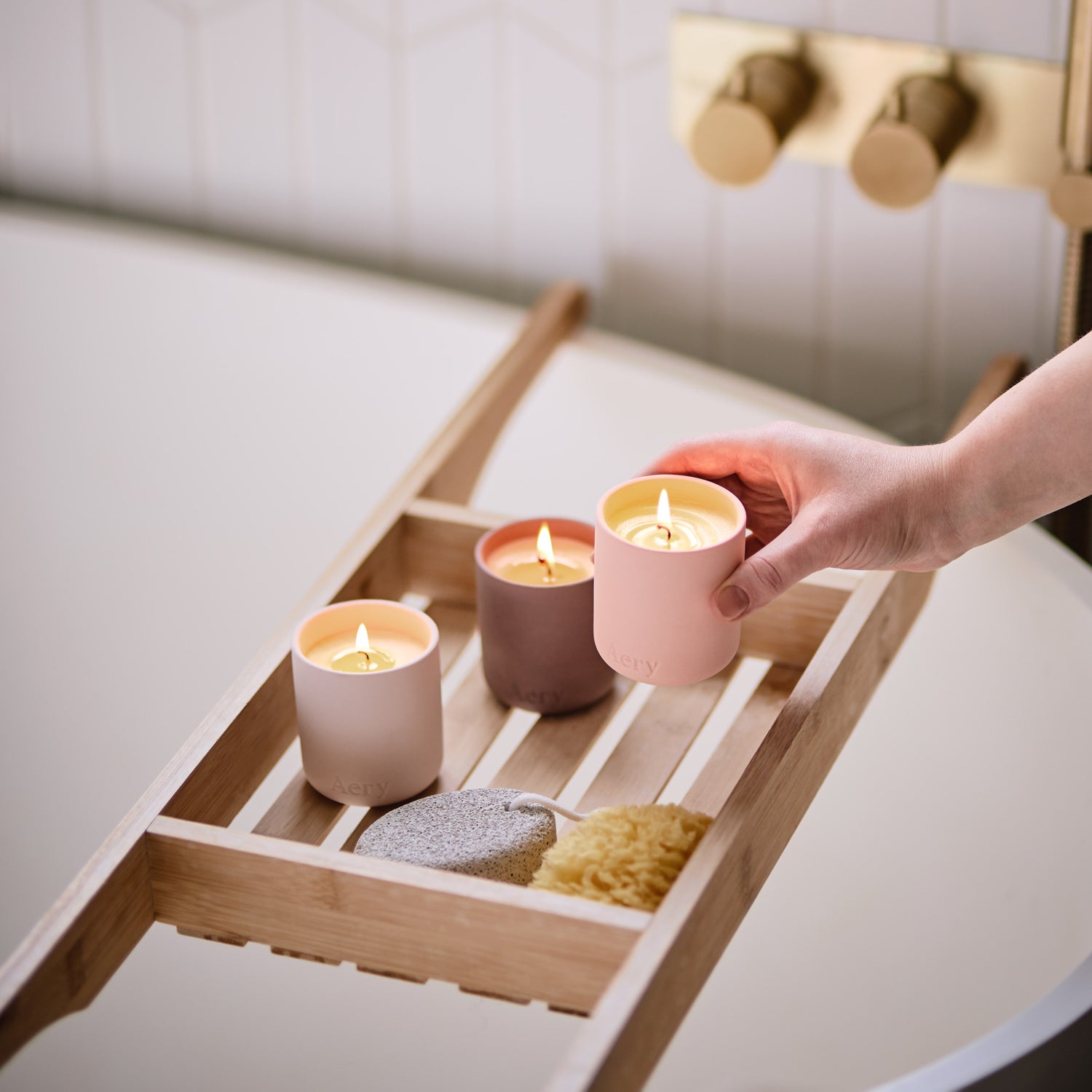 wooden bath caddy with three votive fernweh candles lit with person setting one down