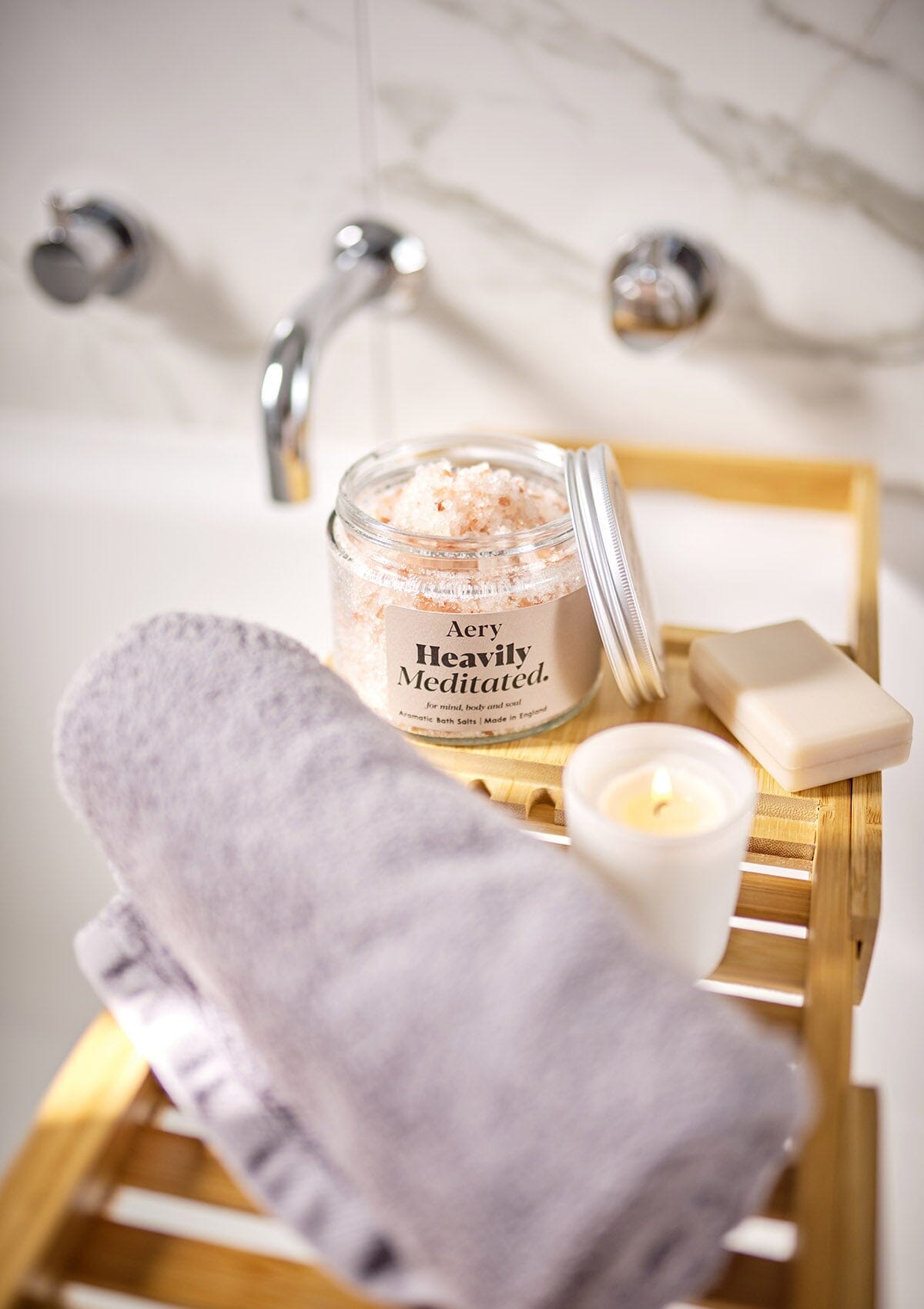 Aery Living Heavily Meditated bath salts with lid off on bath tray with towel soap and candle in bathroom setting