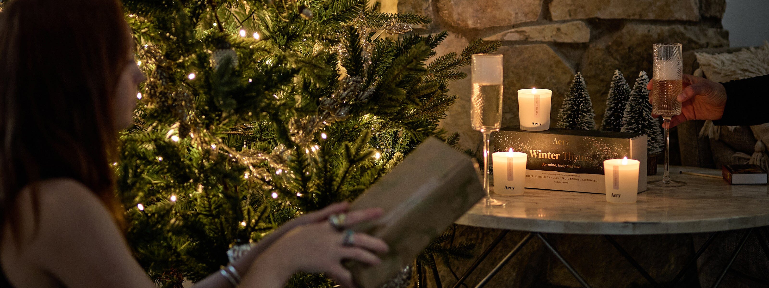 person handing wrapped present to another person infront of a christmas tree