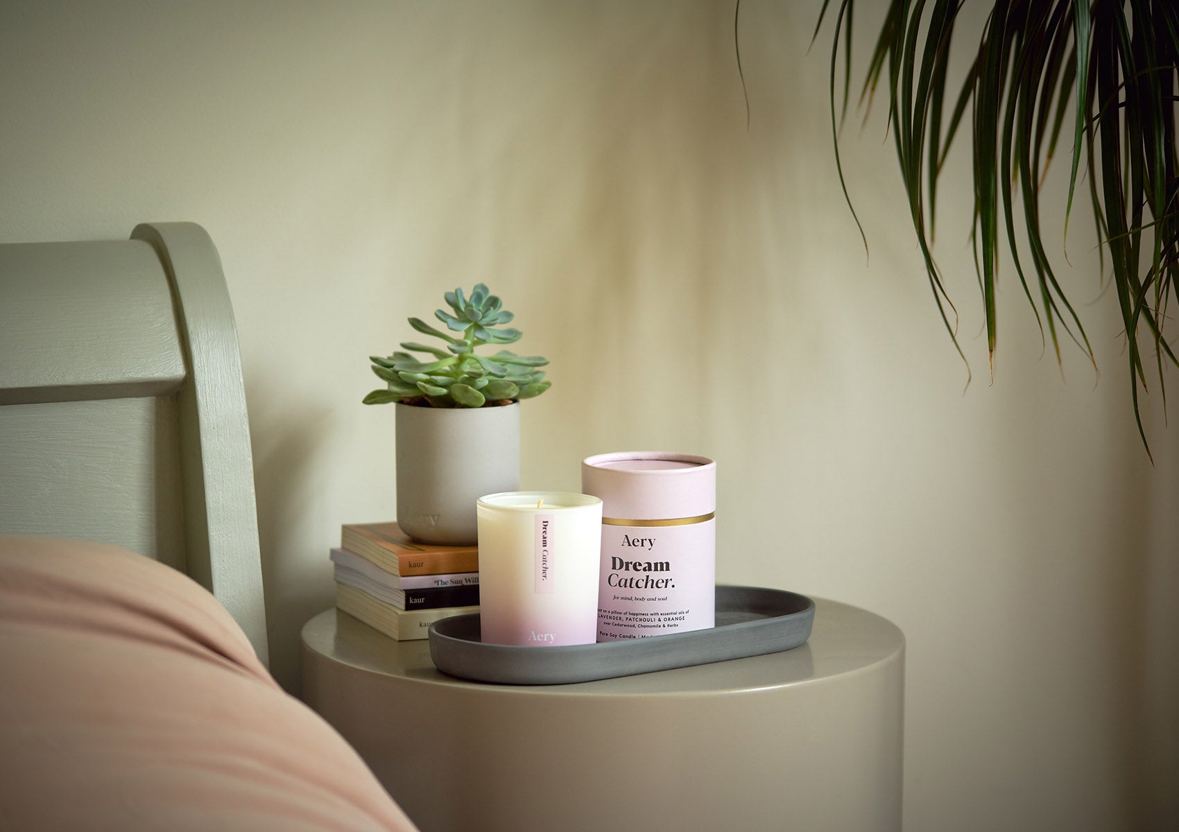 Dream Catcher Scented Candle presented on a bedside table next to a stack of books and a potted plant. 