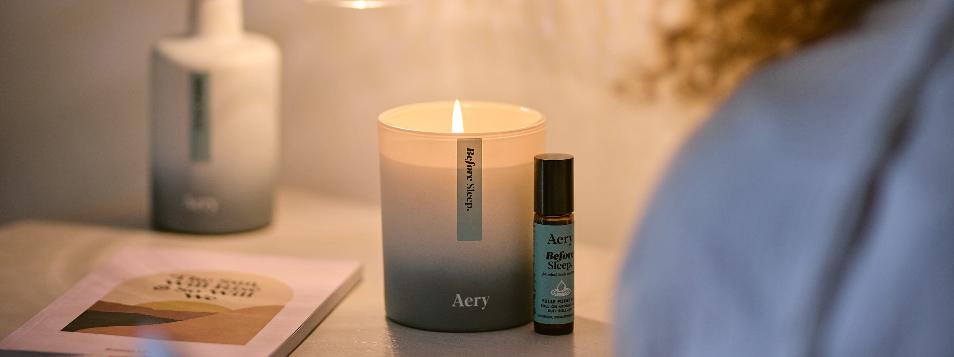 before sleep aery candle displayed next to person reading on a bedside table along with matching diffuser and pulse point roll on