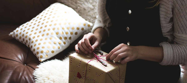 person adding finishing touches to wrapping detail on a Christmas gift, kraft brown paper and candy cane