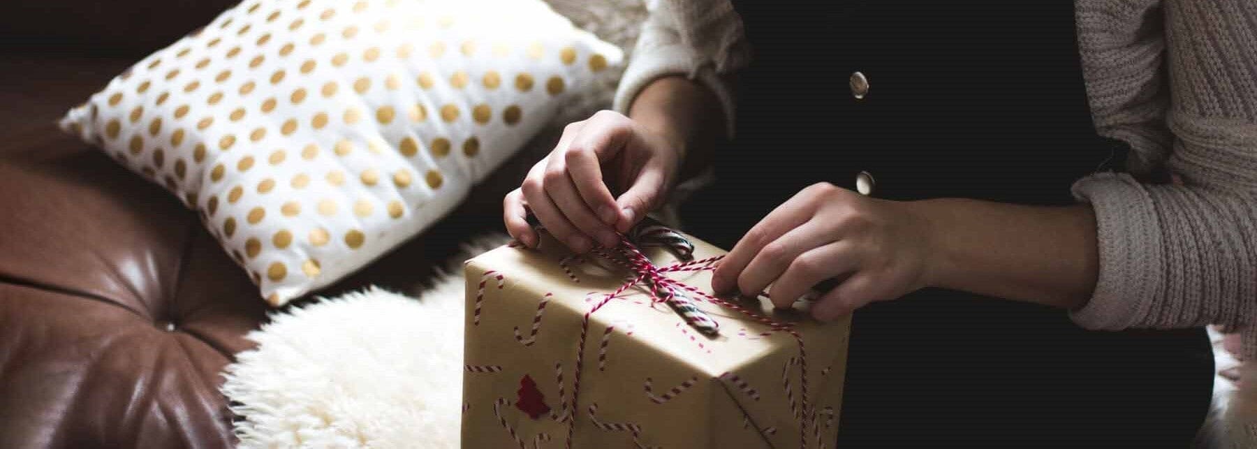 person adding finishing touches to wrapping detail on a Christmas gift, kraft brown paper and candy cane