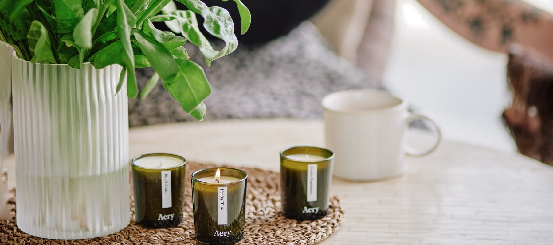 three mini green glass candles on a coffee table next to a vase filled with flowers and a coffee mug