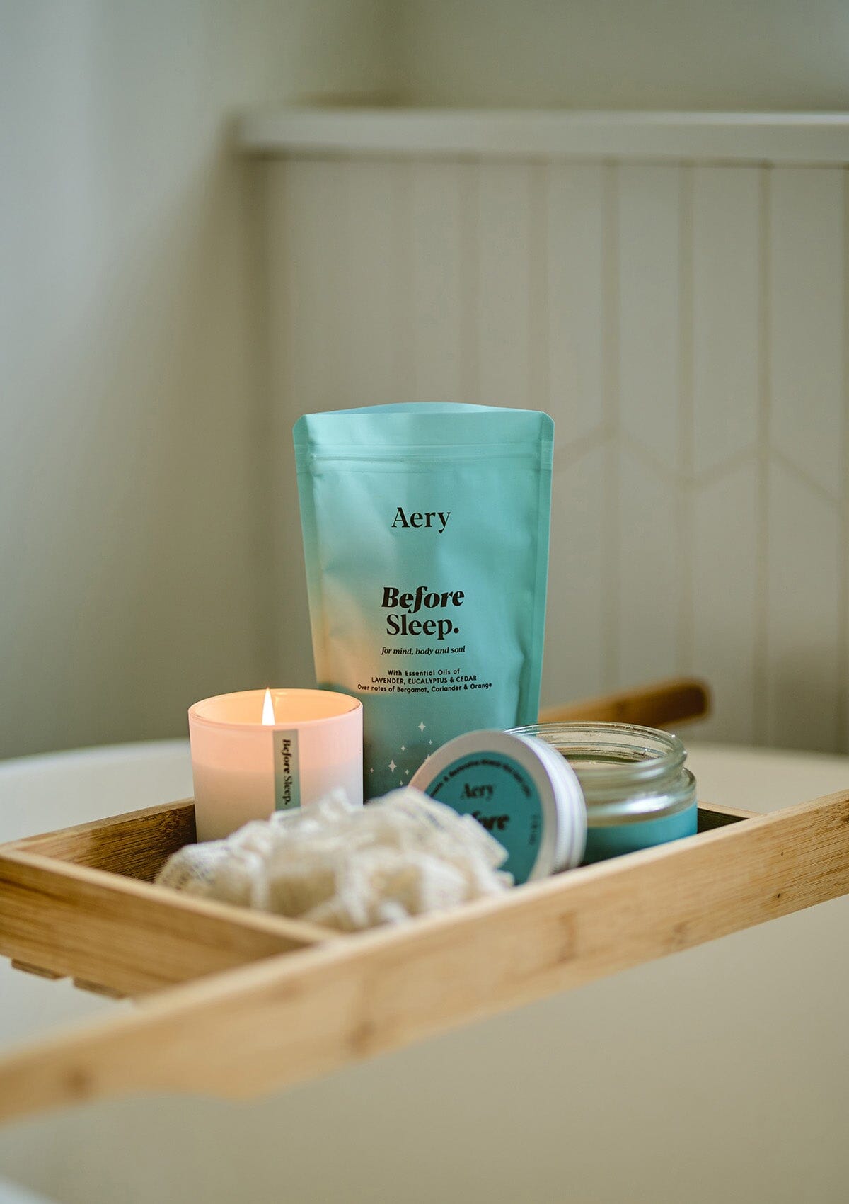 Blue Before Sleep bath salts pouch displayed with Before Sleep candle and bath salts jar placed on wooden bath tray  in bathroom 