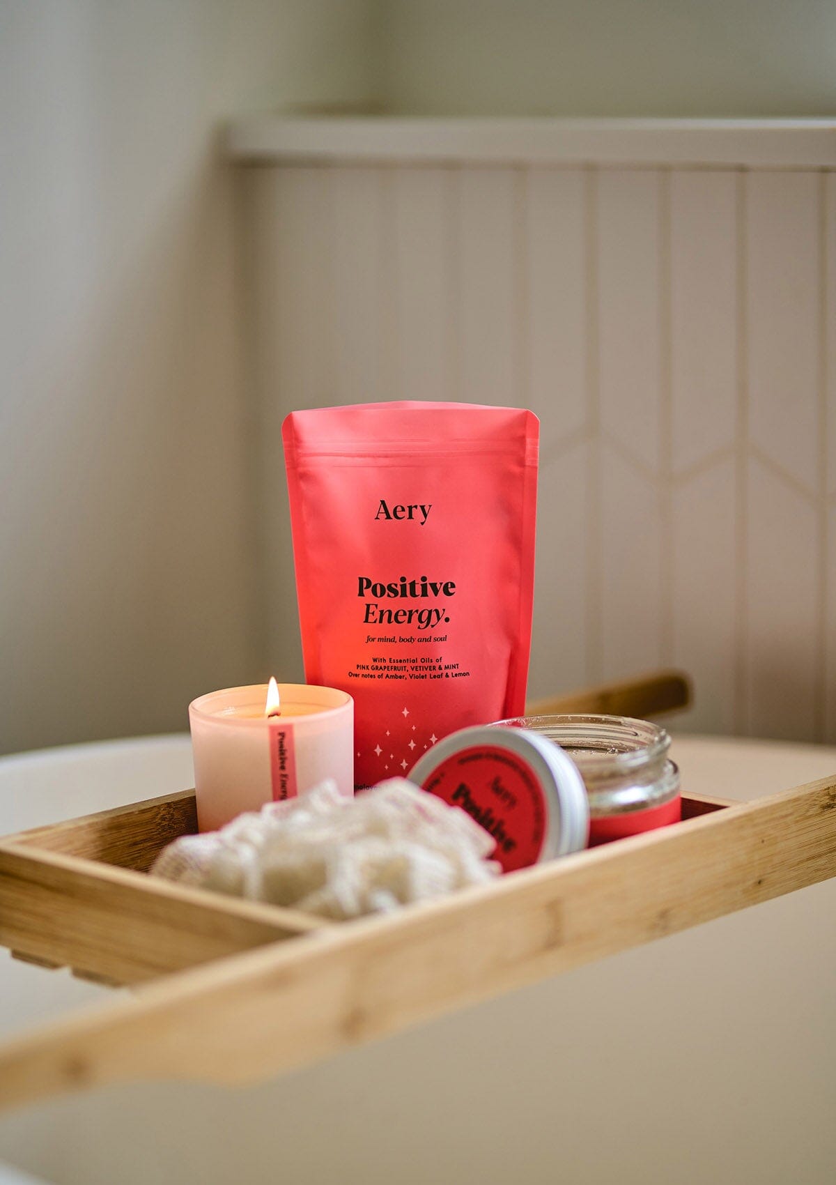 Red Positive Energy by Aery displayed with Positive Energy candle and bath salts jar by Aery placed in wooden bath tray in bathroom 