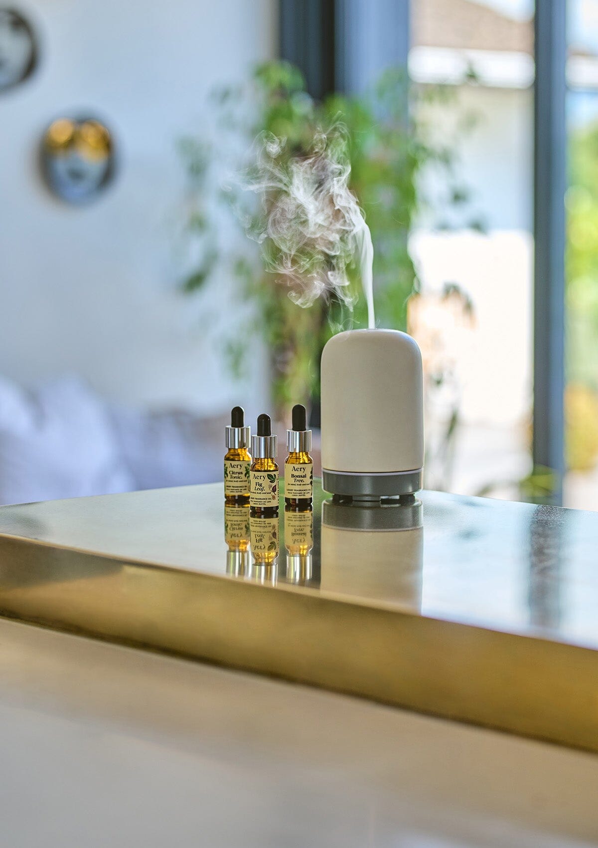 Cream Bonsai Tree, Fig Leaf and Citrus Tonic fragrance oils displayed next to electric diffuser on gold kitchen worktop