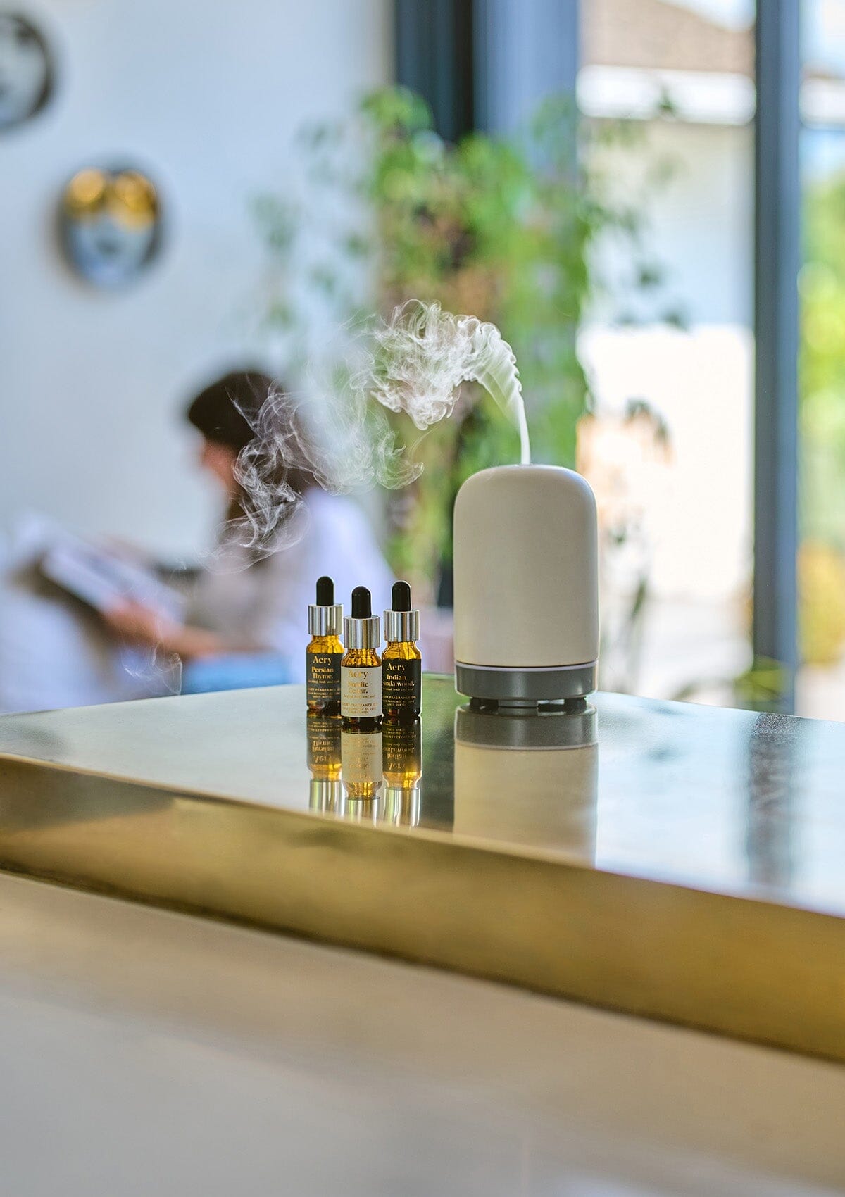 Grey Persian Thyme fragrance oil by Aery displayed next to Indian Sandalwood and Nordic Cedarleaf fragrance oils and electric diffuser placed on gold kitchen worktop