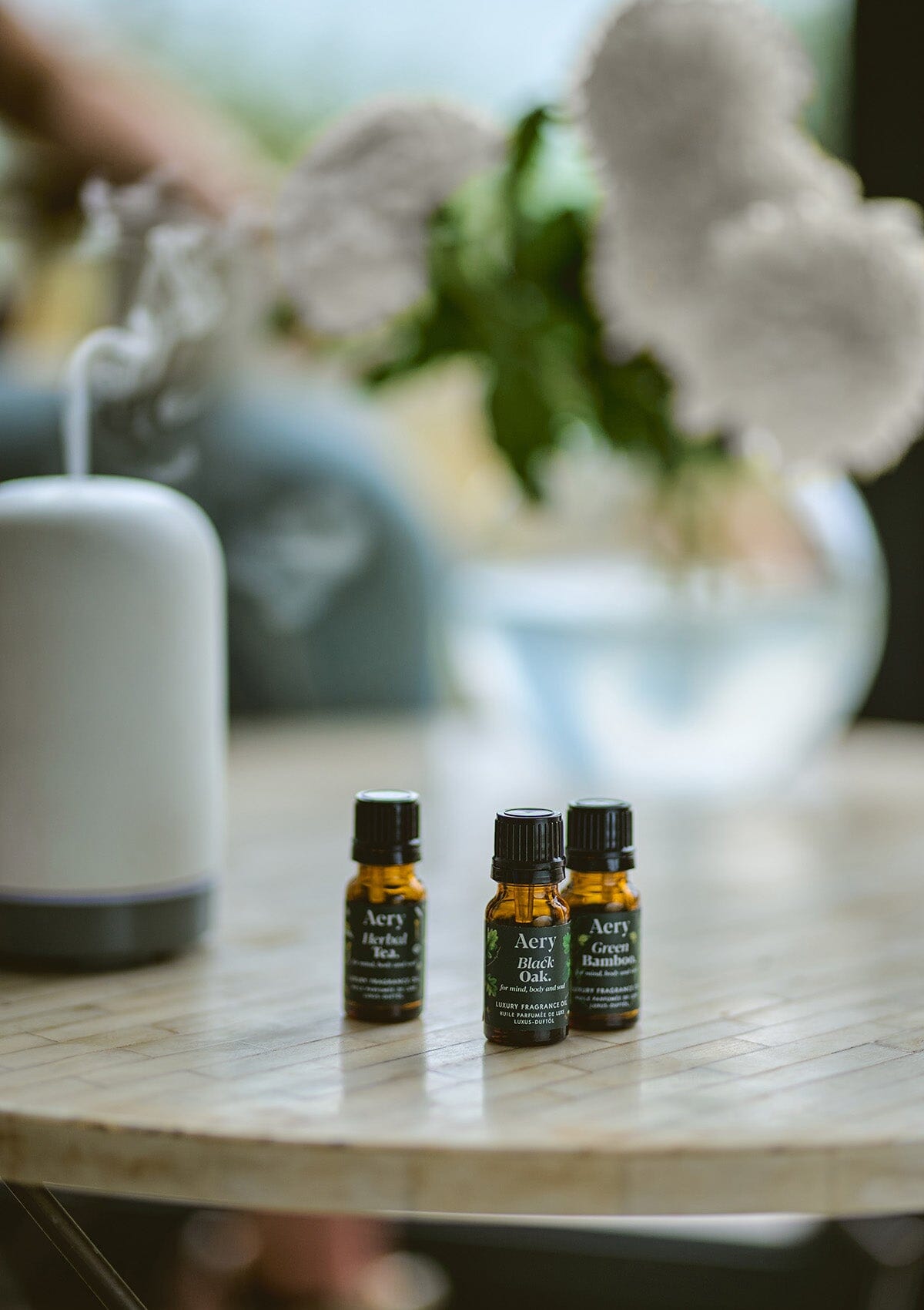 Green Botanical set of three fragrance oils by Aery displayed next to electric diffuser and vase of flowers placed on round table 