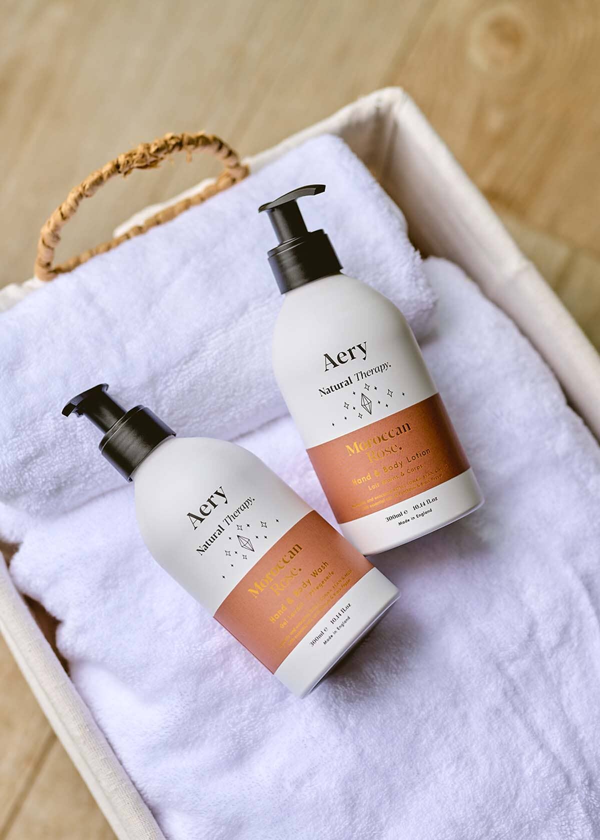 Aubergine Moroccan Rose hand and body wash and lotion duo by Aery displayed on white towel in basket