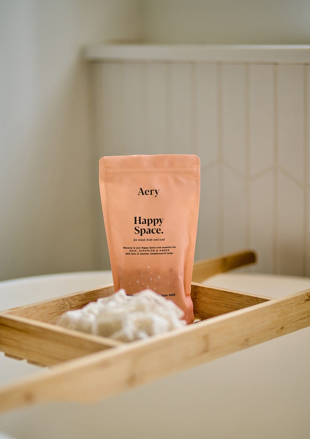 Pink Happy Space bath salts pouch displayed on wooden bath tray in bathroom 