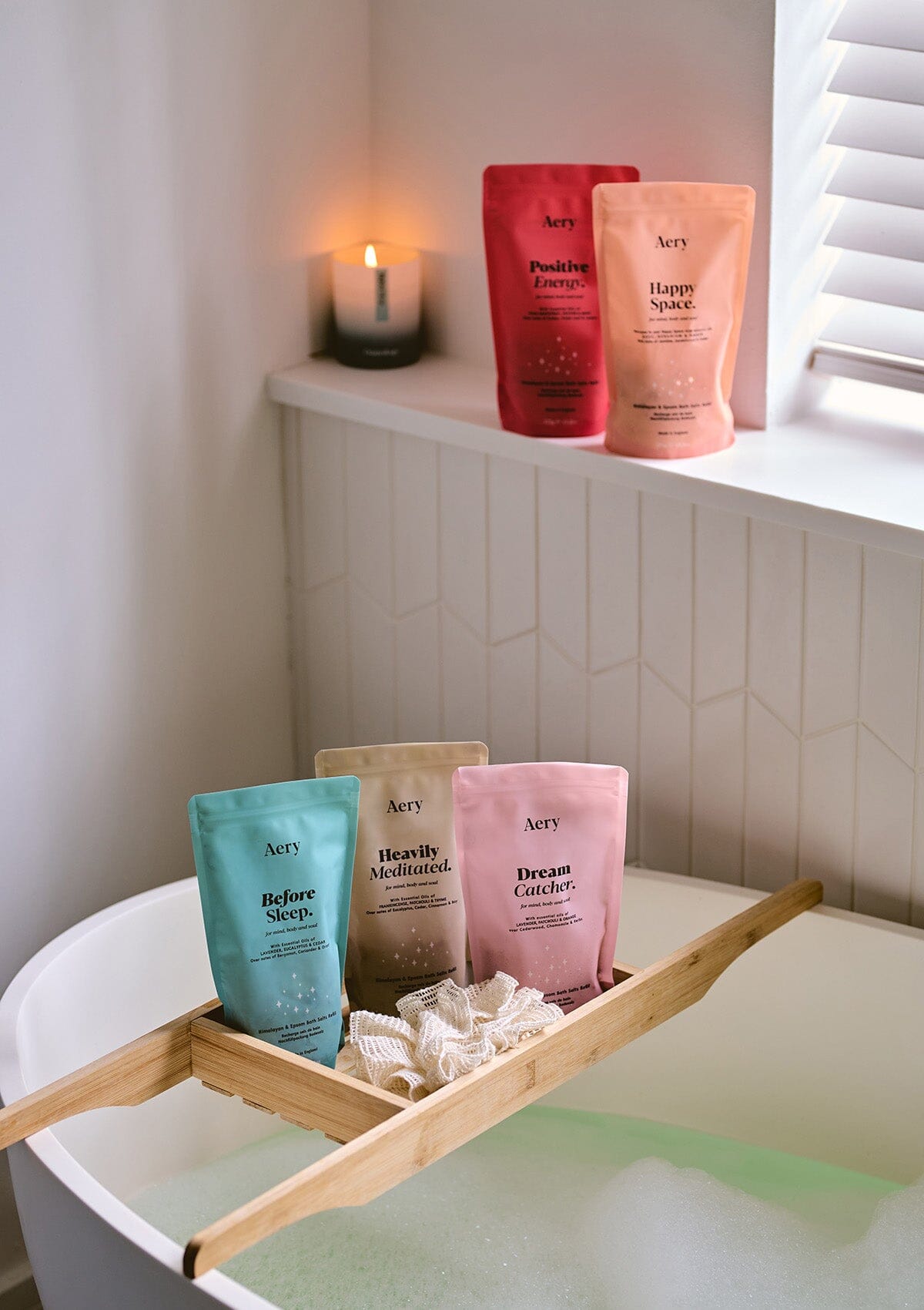Collection of Aromatherapy bath salt pouches by Aery displayed with before sleep candle in bath room with  bathtub 