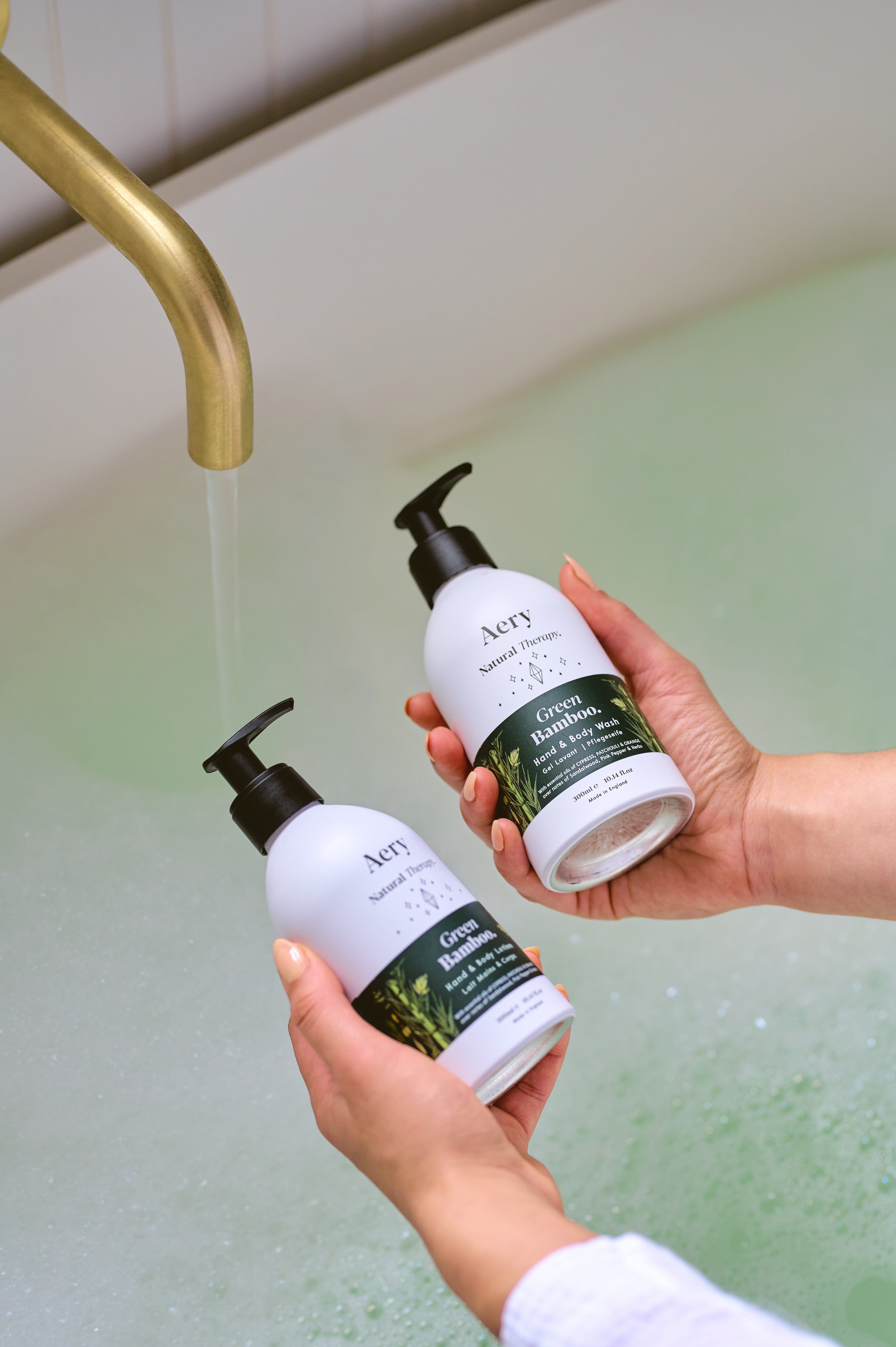 Green Bamboo hand and body wash and lotion duo by Aery displayed in hands over bubble bath