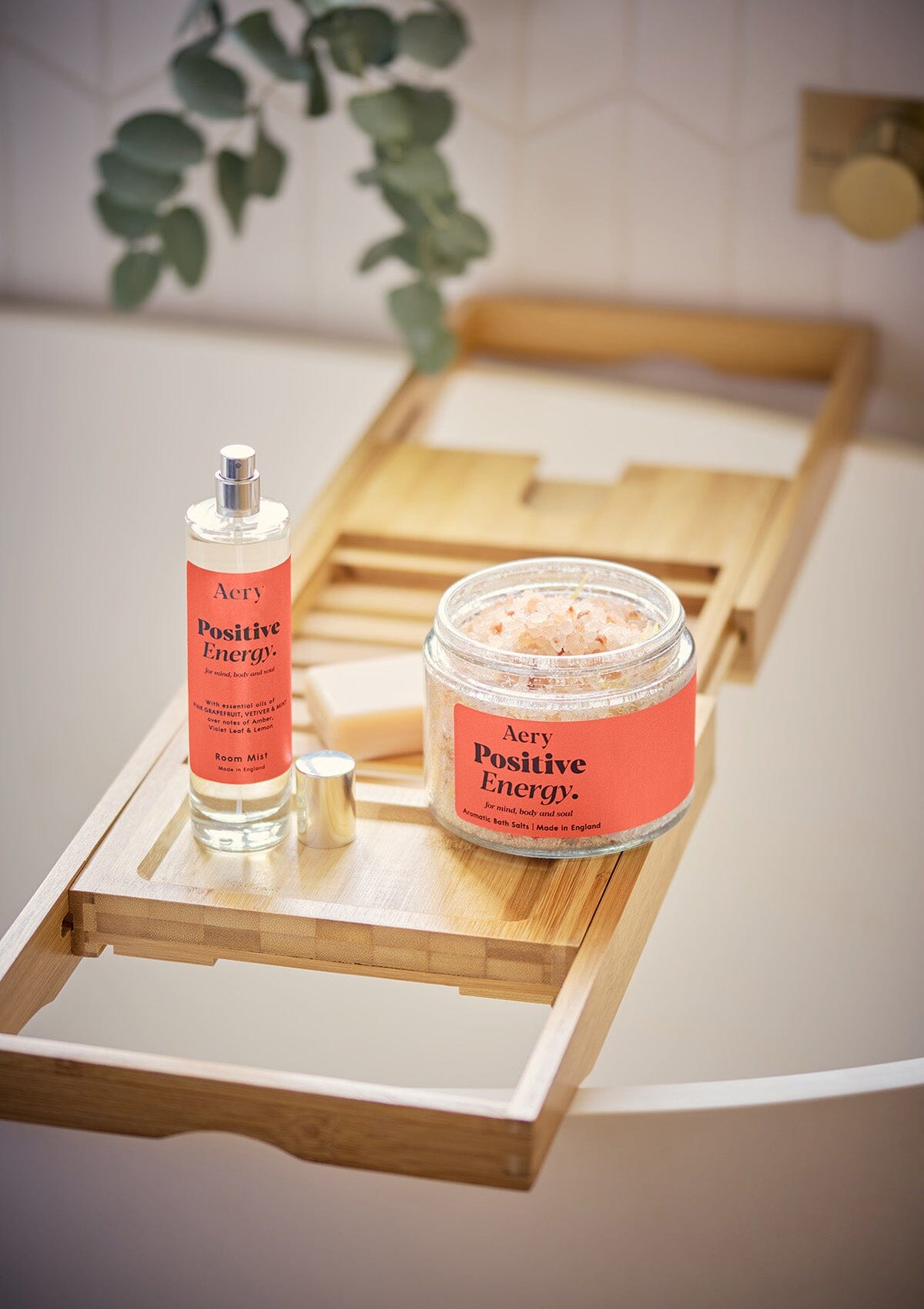 Red Positive Energy bath Salts by Aery displayed with Positive Energy room mist placed on wooden tray over bath tub in bathroom 