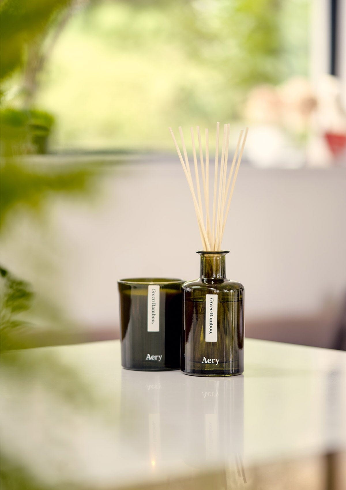 green bamboo candle by aery displayed next to green bamboo diffuser by aery displayed on white kitchen worktop
