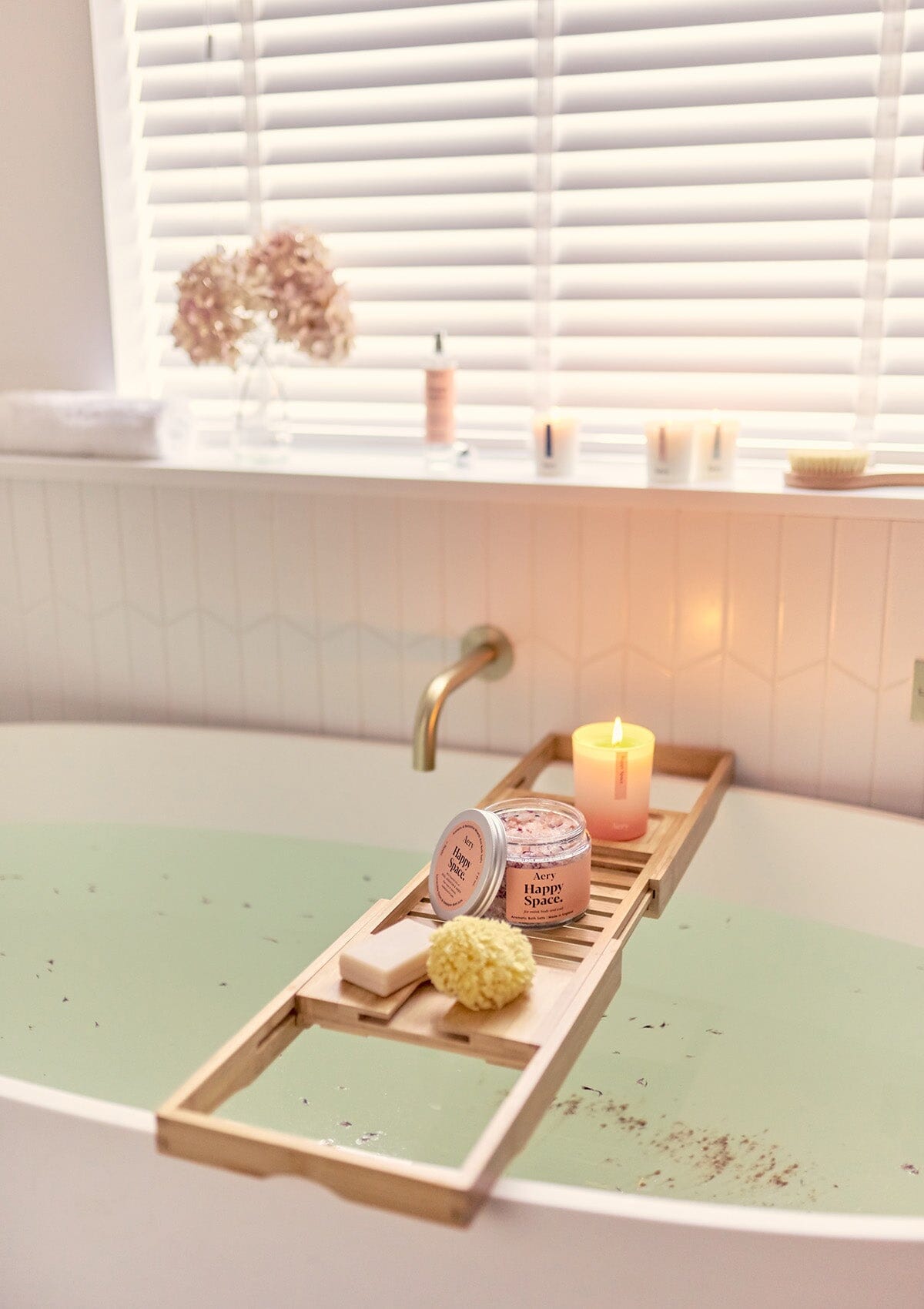 Pink Happy Space bath salts by Aery displayed next to Happy Space candle on wooden bath tray in bathroom 