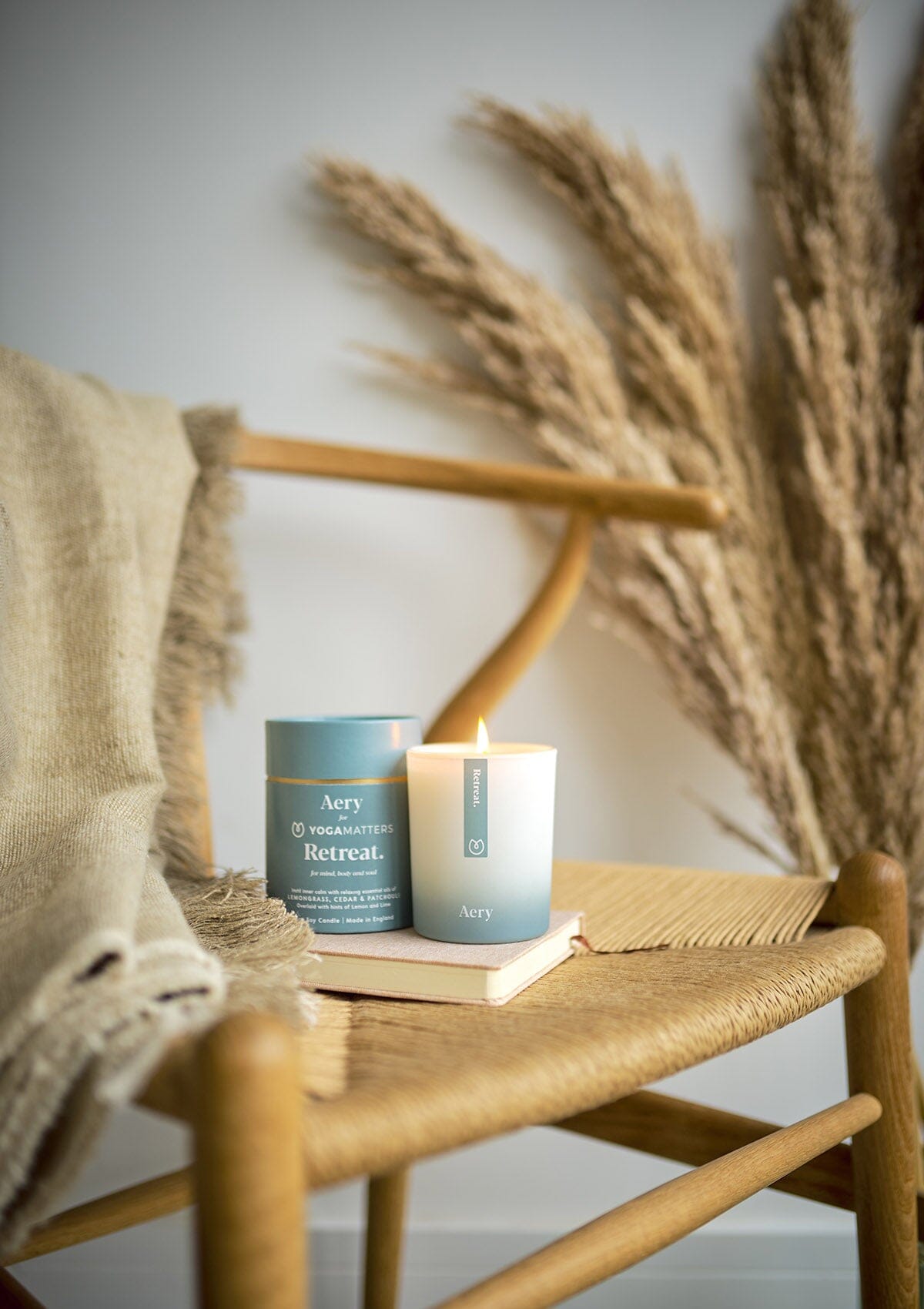 Blue Retreat candle by Aery displayed next to product packaging on wicker chair 