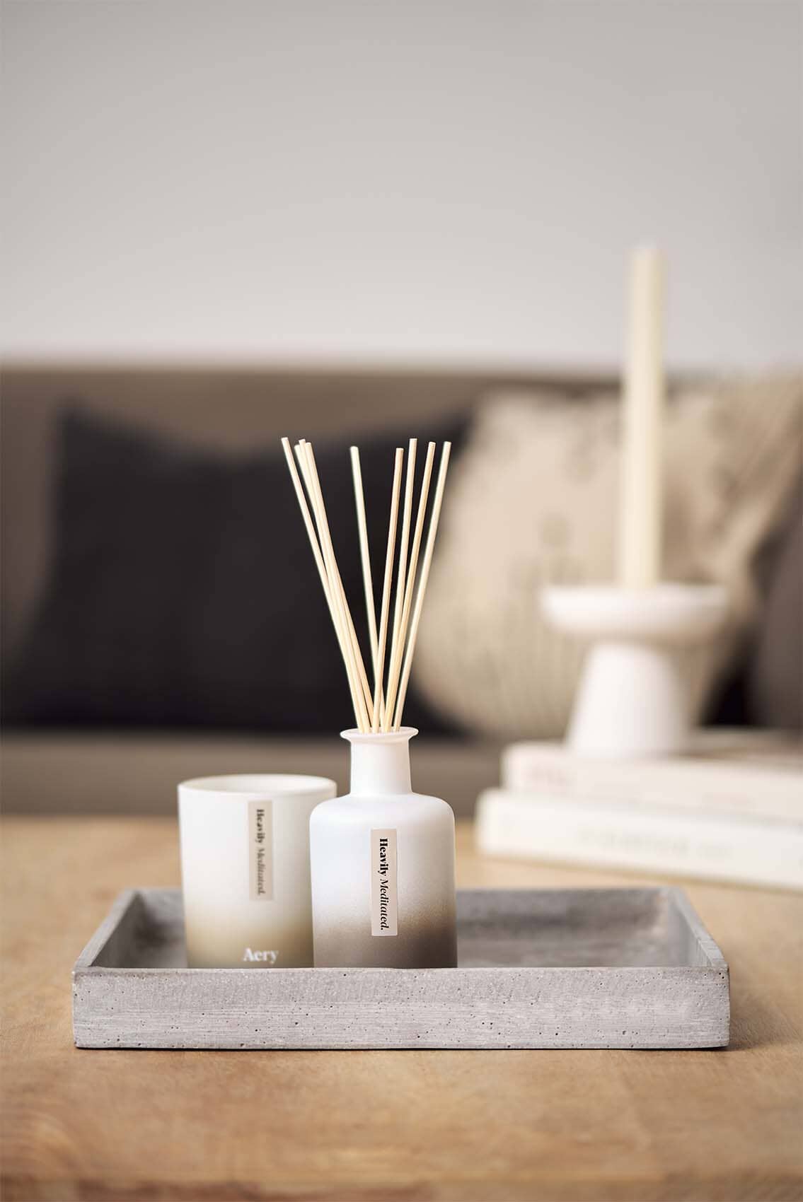 Beige Heavily Meditated diffuser by Aery displayed next to Heavily Meditated candle placed in grey tray on brown table 