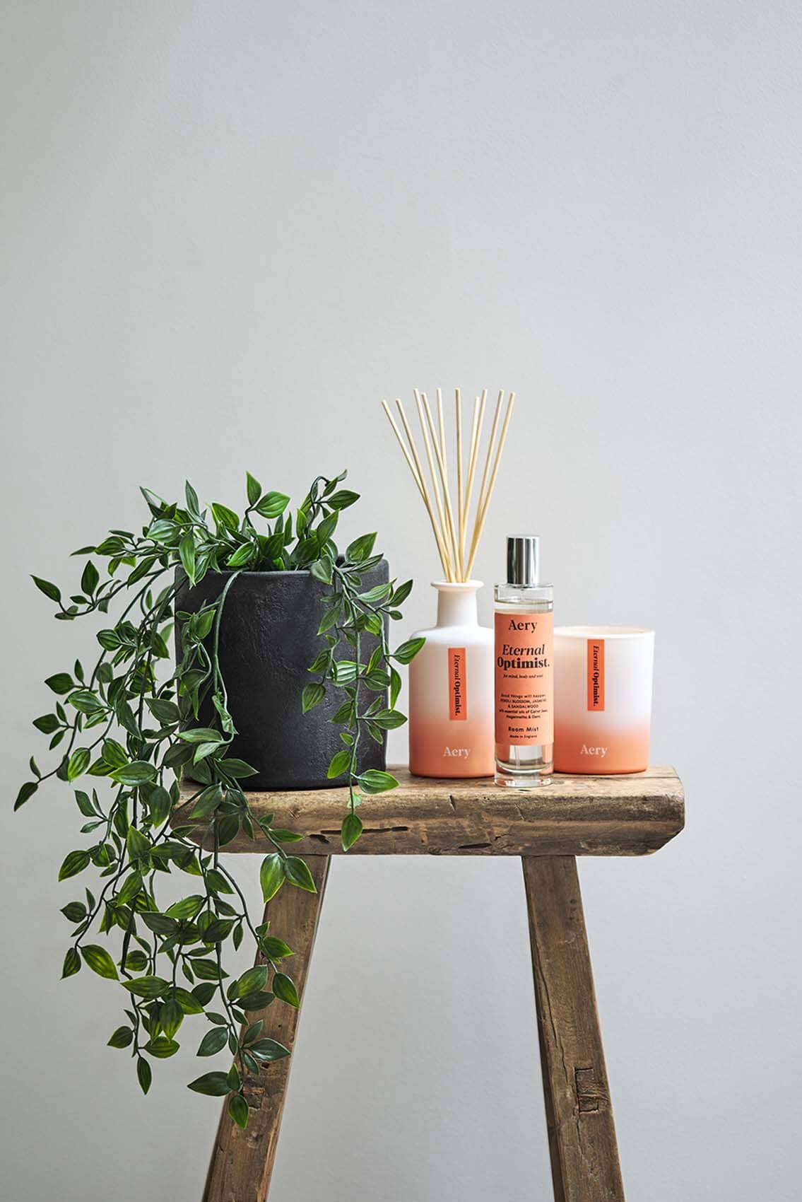 Orange Eternal Optimist diffuser displayed with Eternal Optimist room mist and candle and potted plant placed on wooden stall