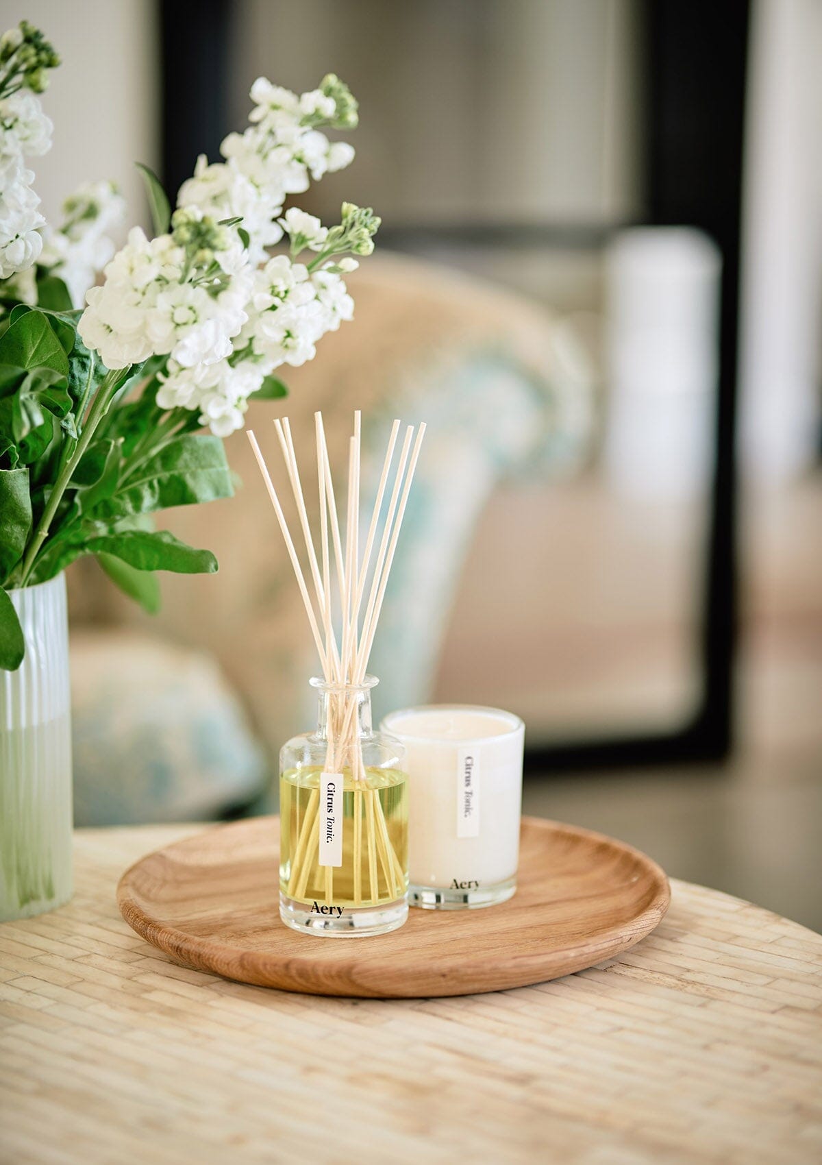 Citrus Tonic diffuser displayed next to citrus tonic candle placed on wooden table next to vase of flowers 