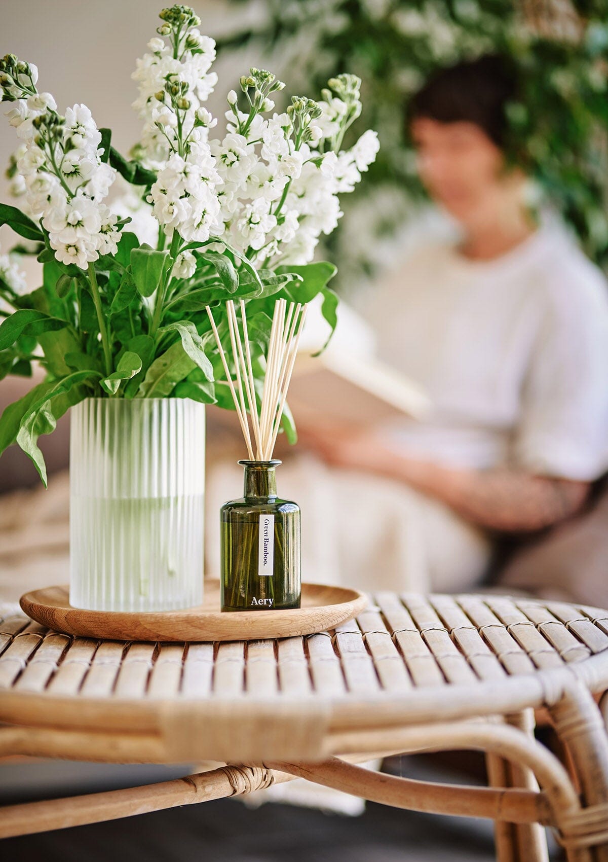 Green Bamboo diffuser by aery displayed next to glass vase of white flowers 