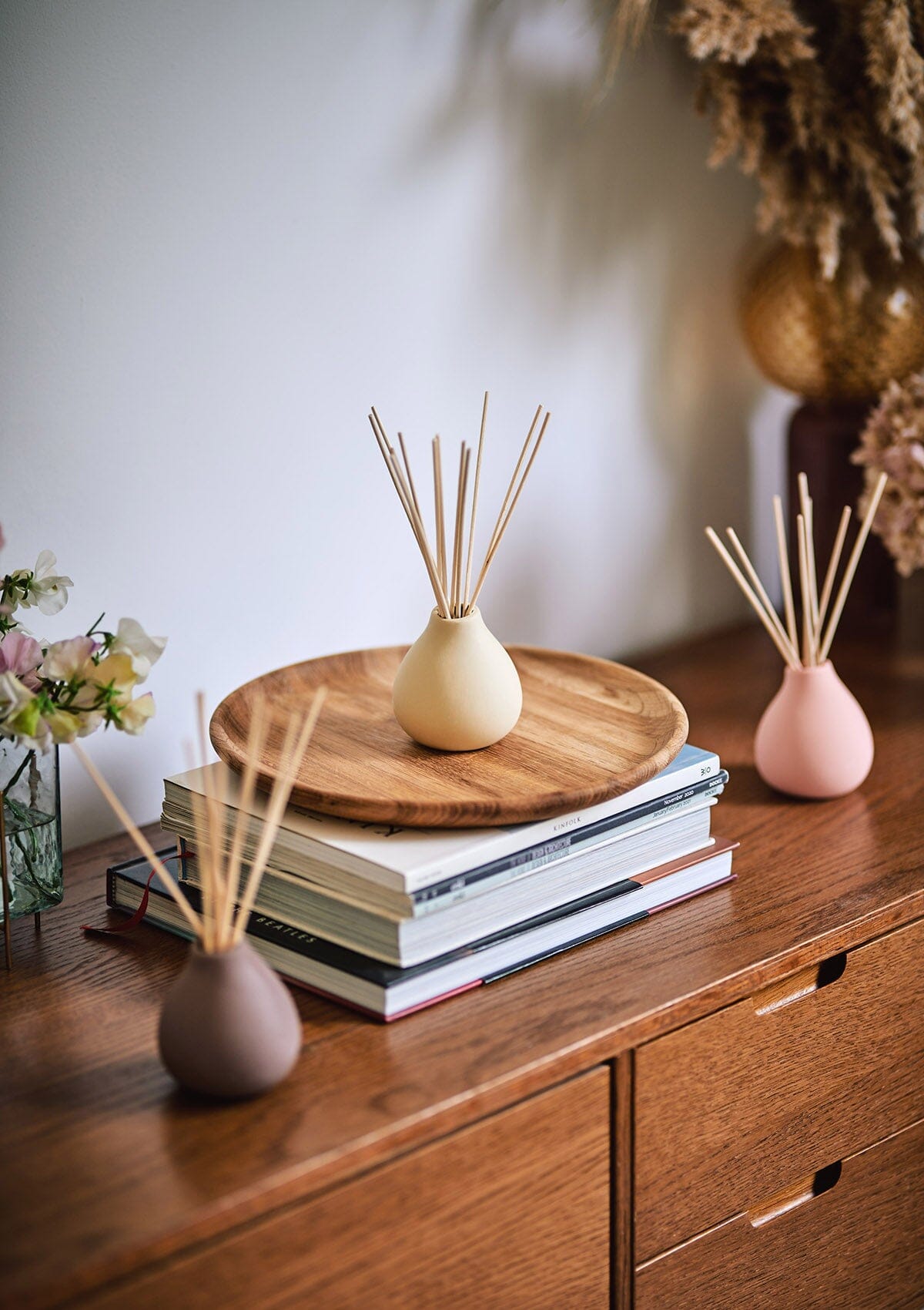 Cream Himalayan Diffuser by Aery displayed on pile of books on wooden shelf with vase of flowers 