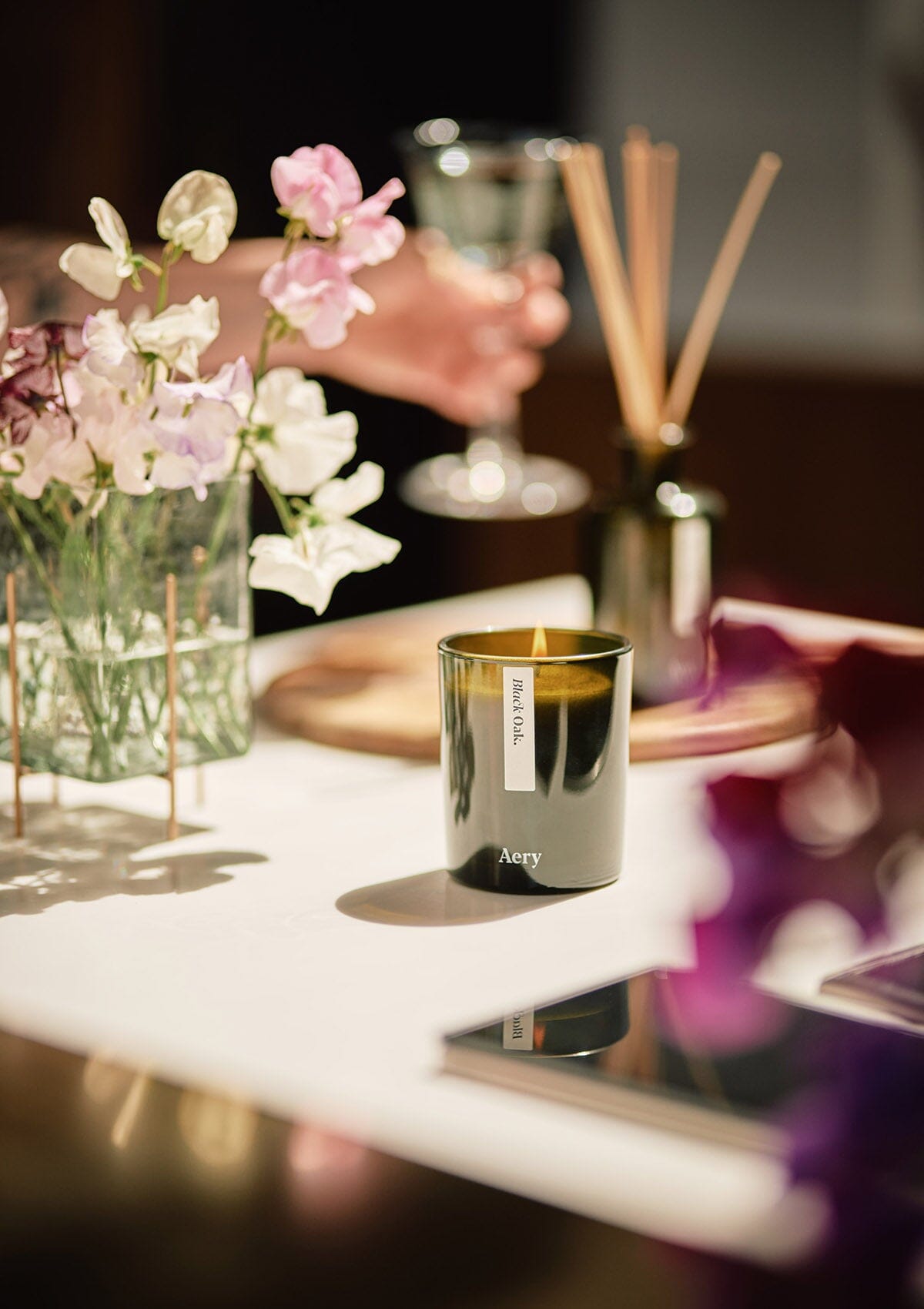 Green Black Oak candle by Aery displayed next to vase of flowers placed on kitchen work top 