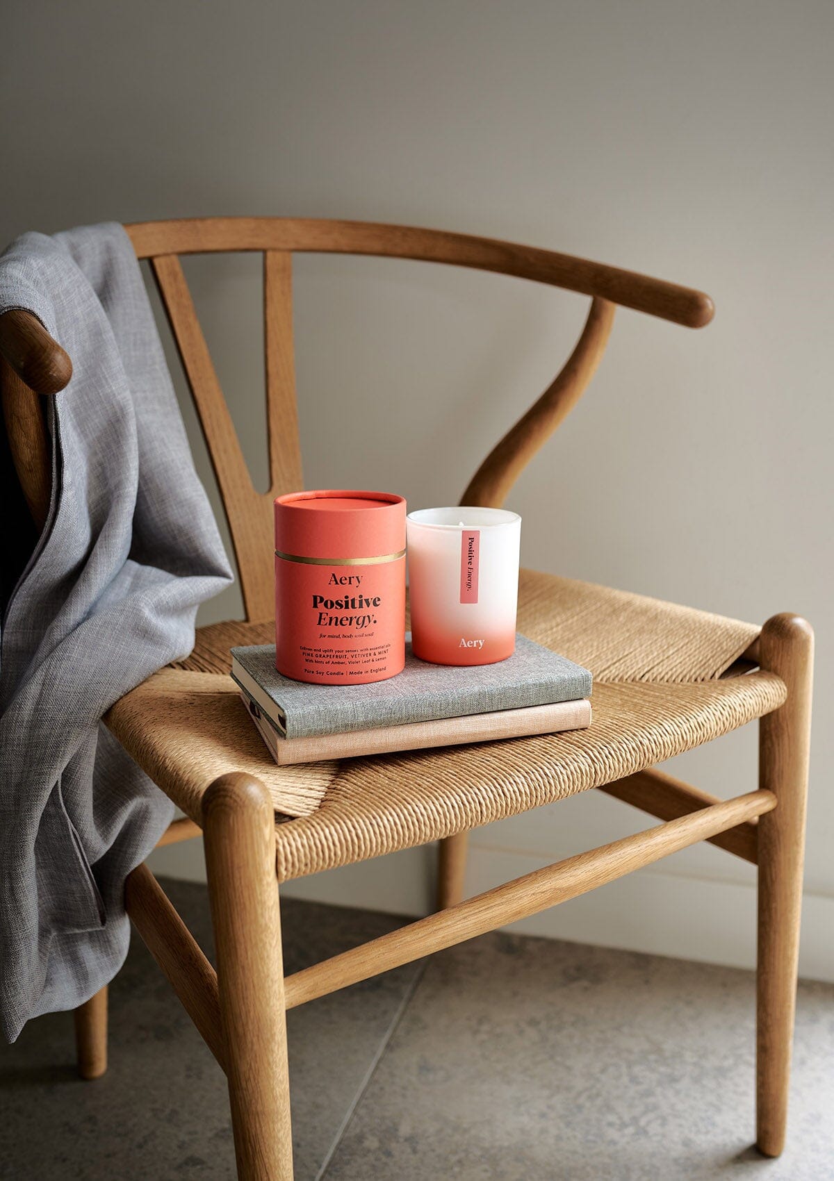 Orange Positive Energy candle displayed next to Product packaging by Aery placed on books and wicker chair 
