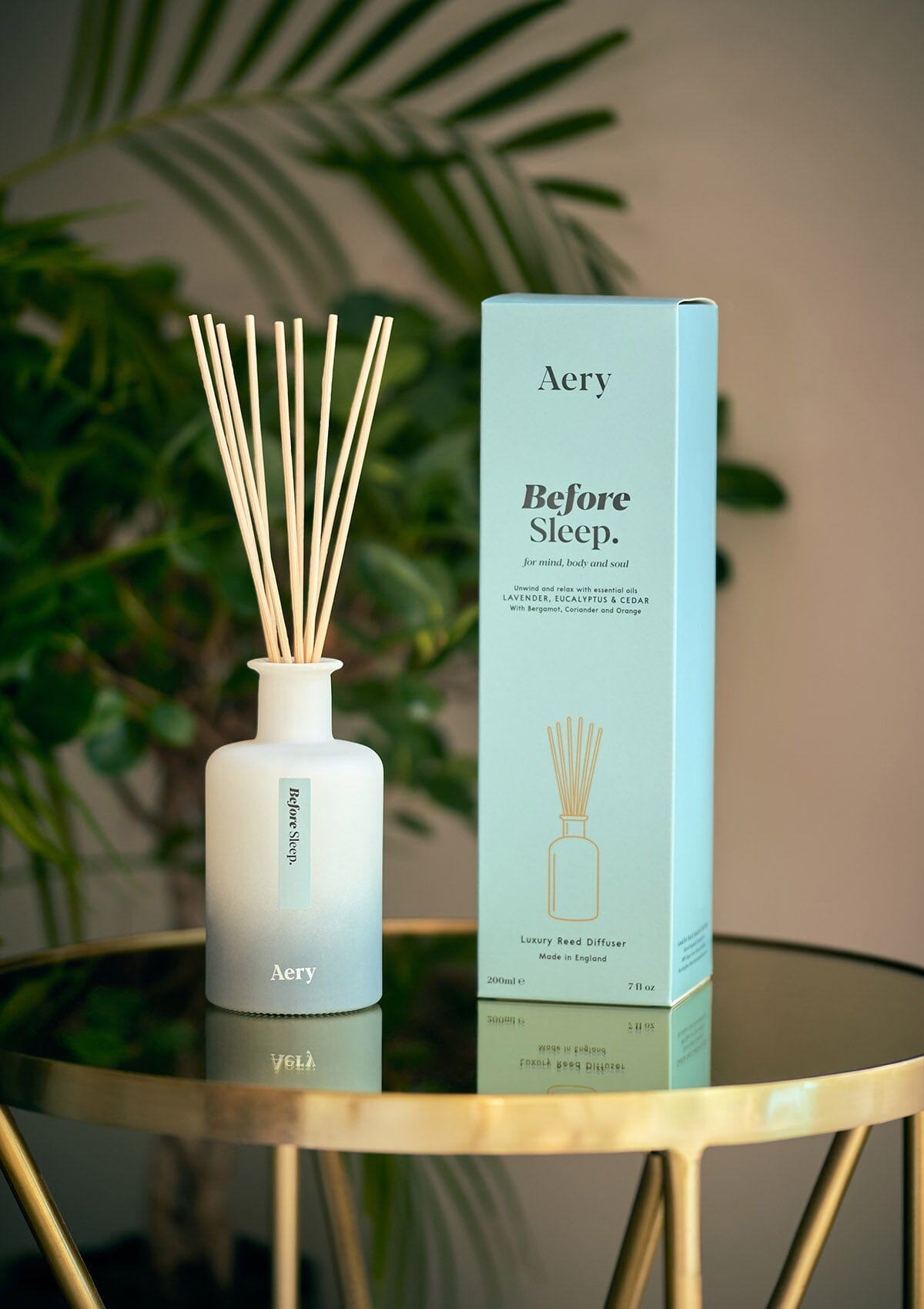 Blue Before Sleep diffuser by Aery displayed next to product packaging on round gold table with green plants 