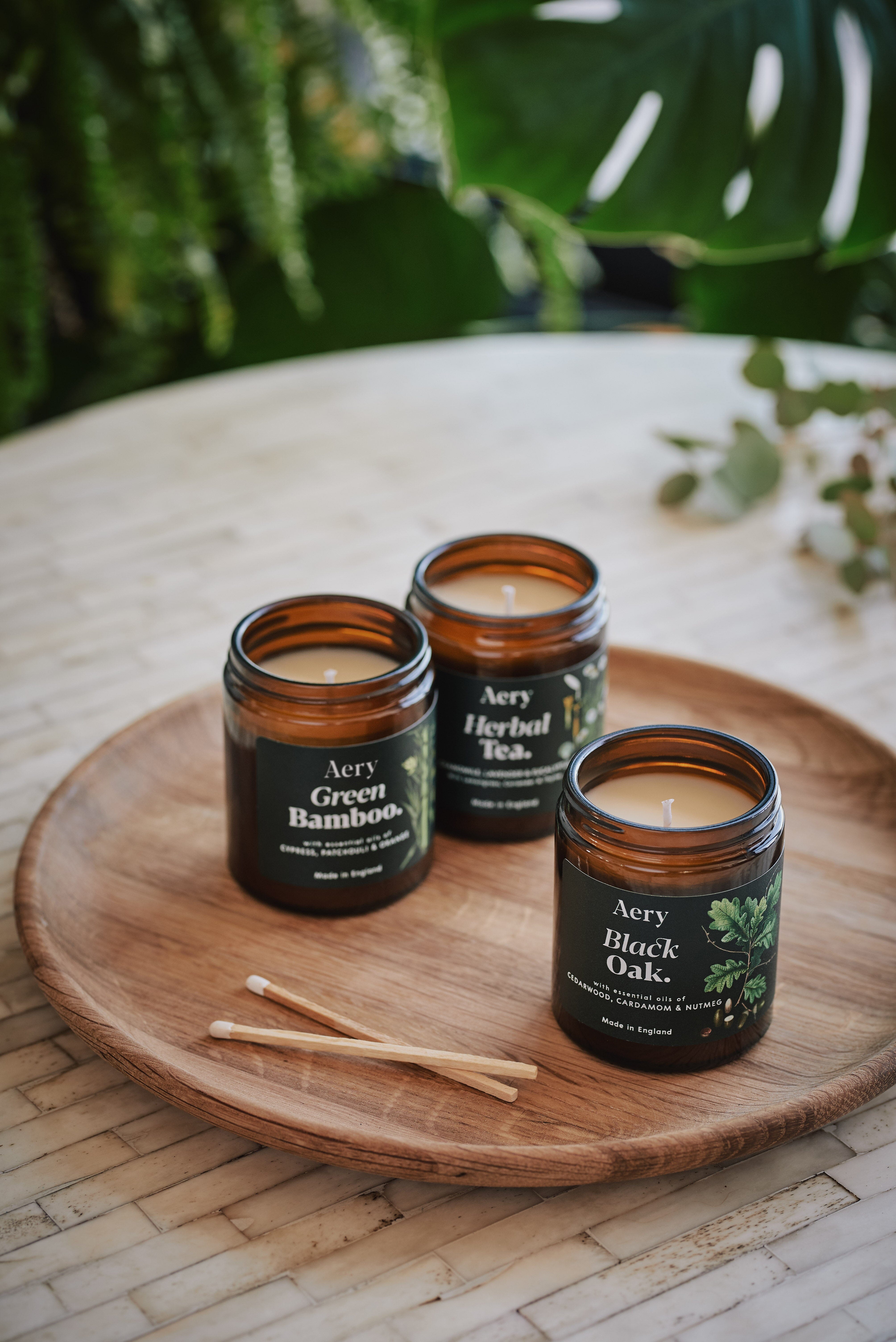 Green Botanical collection of three jar candles by Aery displayed on wooden circle tray with match sticks 