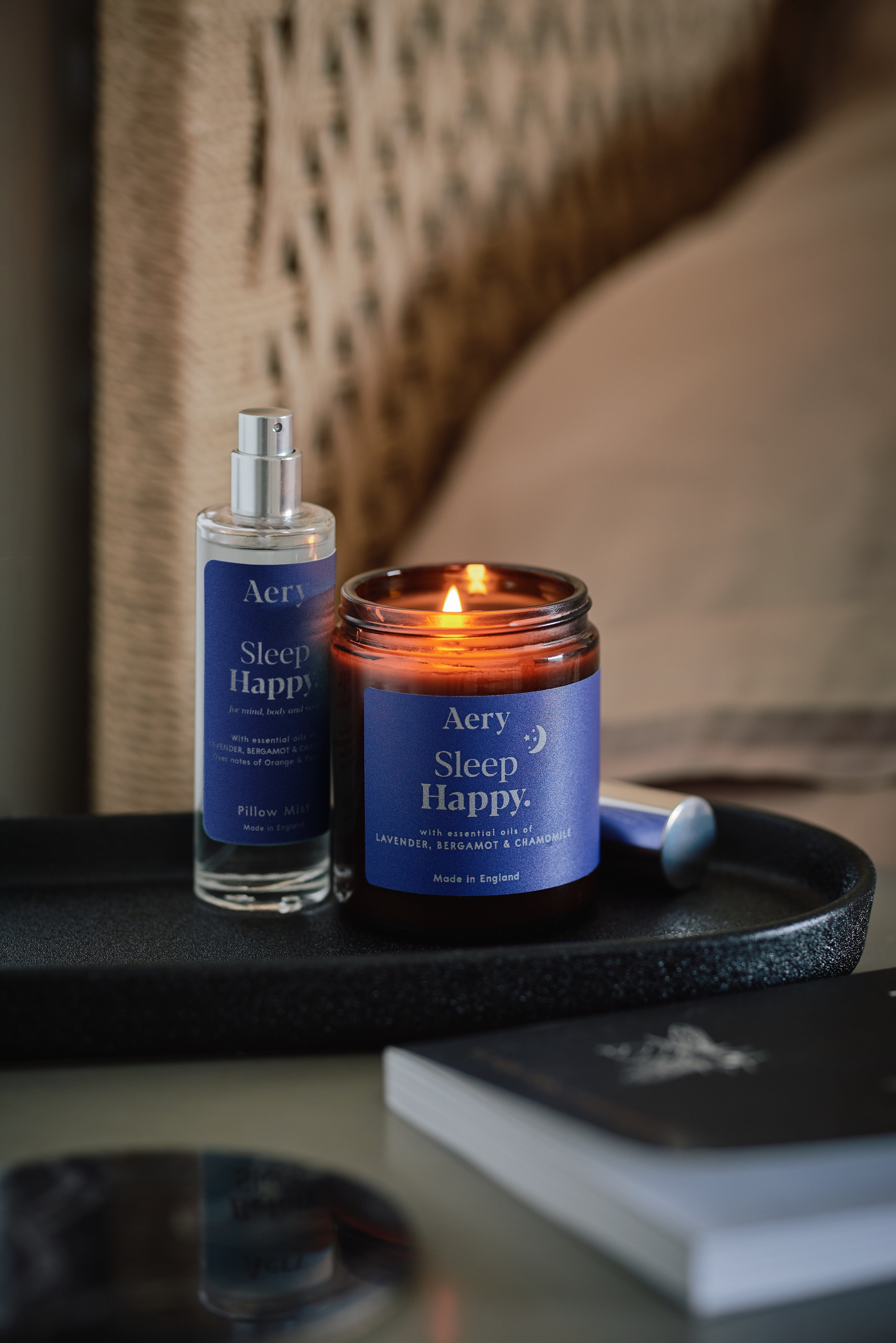 Blue Sleep Happy pillow mist by Aery displayed next to sleep happy jar candle on bedside table  
