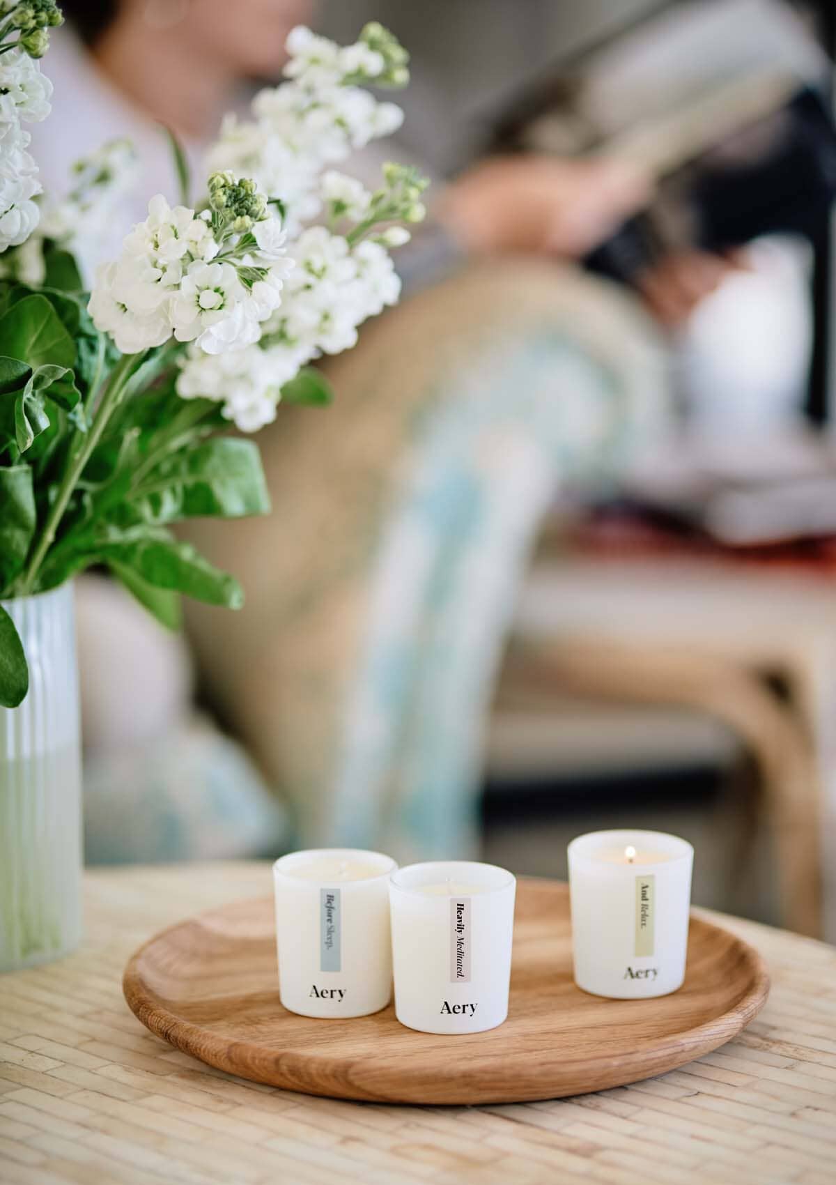 Beige Heavily Mediated gift set of three candles by aery displayed next to white flowers placed on wooden tray 