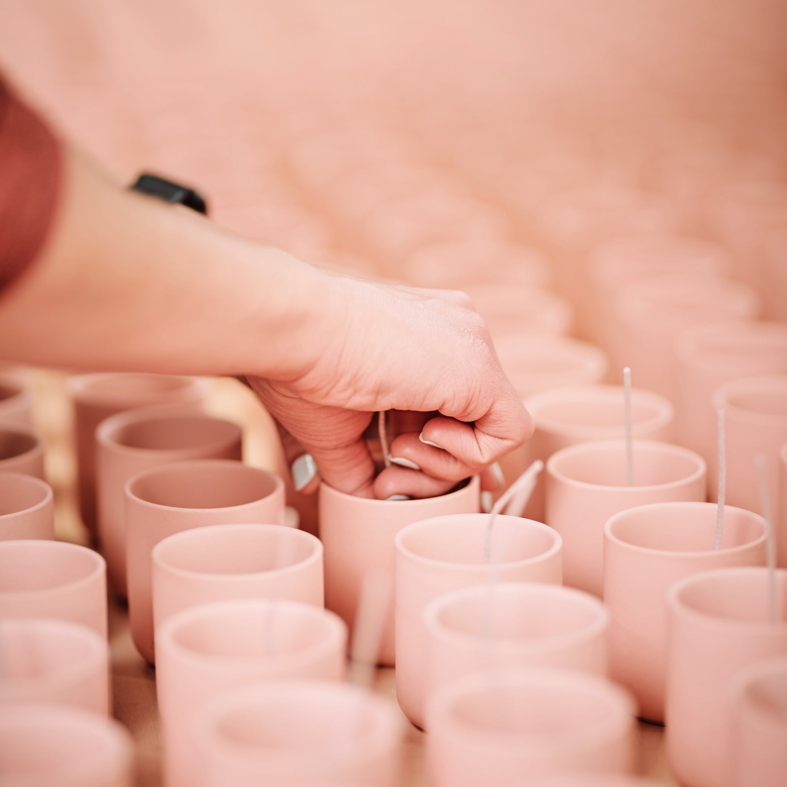 persons hand sticking wicks in candle vessels ready for candle making