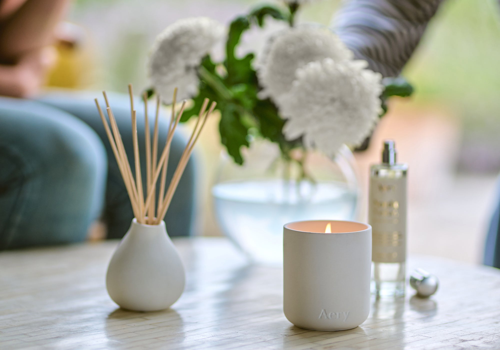 a collection of nordic cedar scented candle, diffuser and room mist by aery living displayed on a coffee table with bunch of flowers in the background