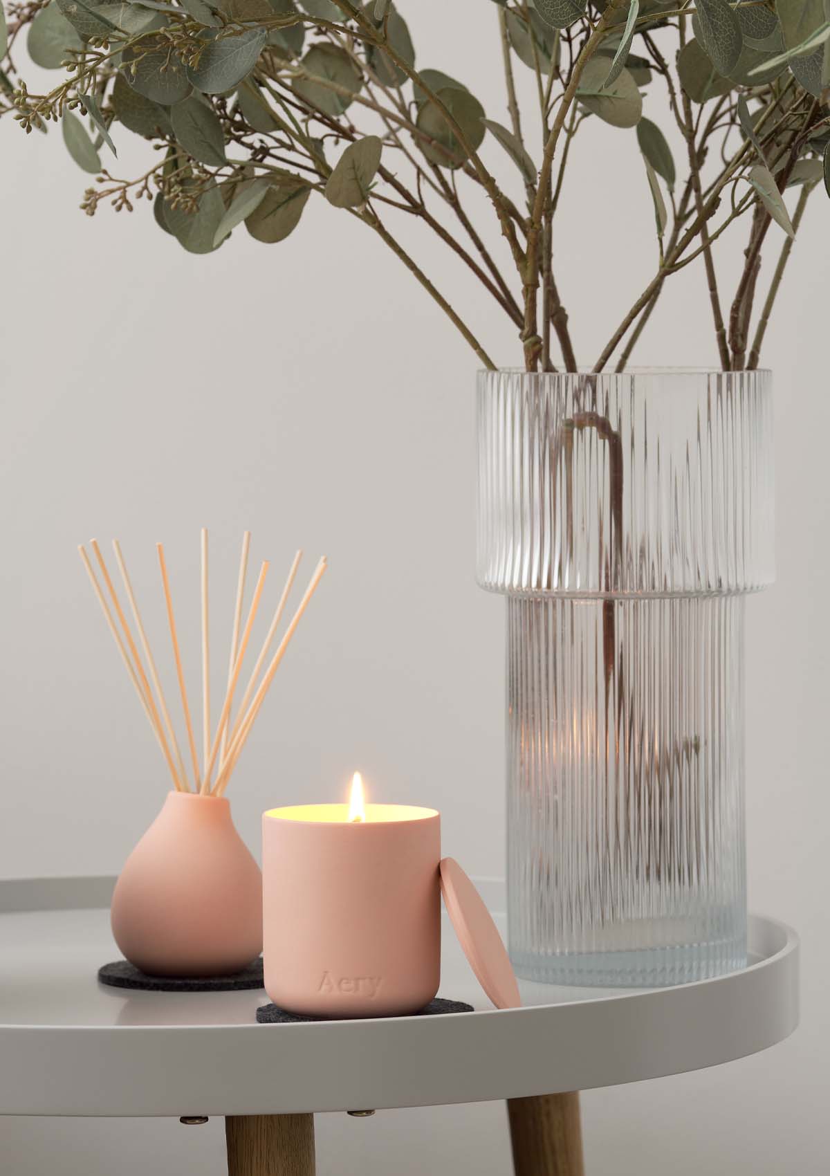 Peach Aztec Tuberose Candle and Diffuser by Aery displayed next to glass vase of greenery on grey circle table 