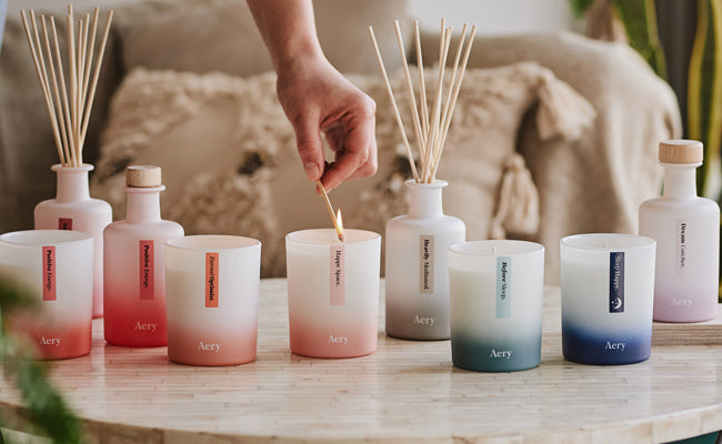 collection of aery living aromatherapy candles and diffusers displayed on a coffee table whilst person lights happy space candle