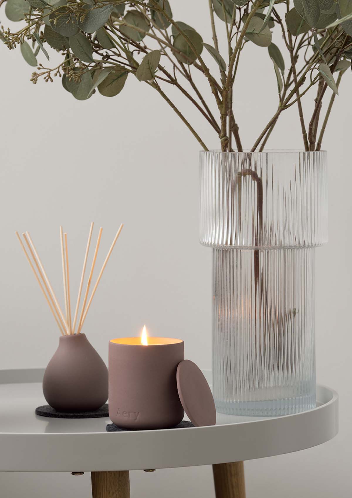 Aubergine moroccan Rose candle by Aery  displayed next to Aubergine Moroccan Rose reed diffuser by Aery and glass vase placed on grey circle table 