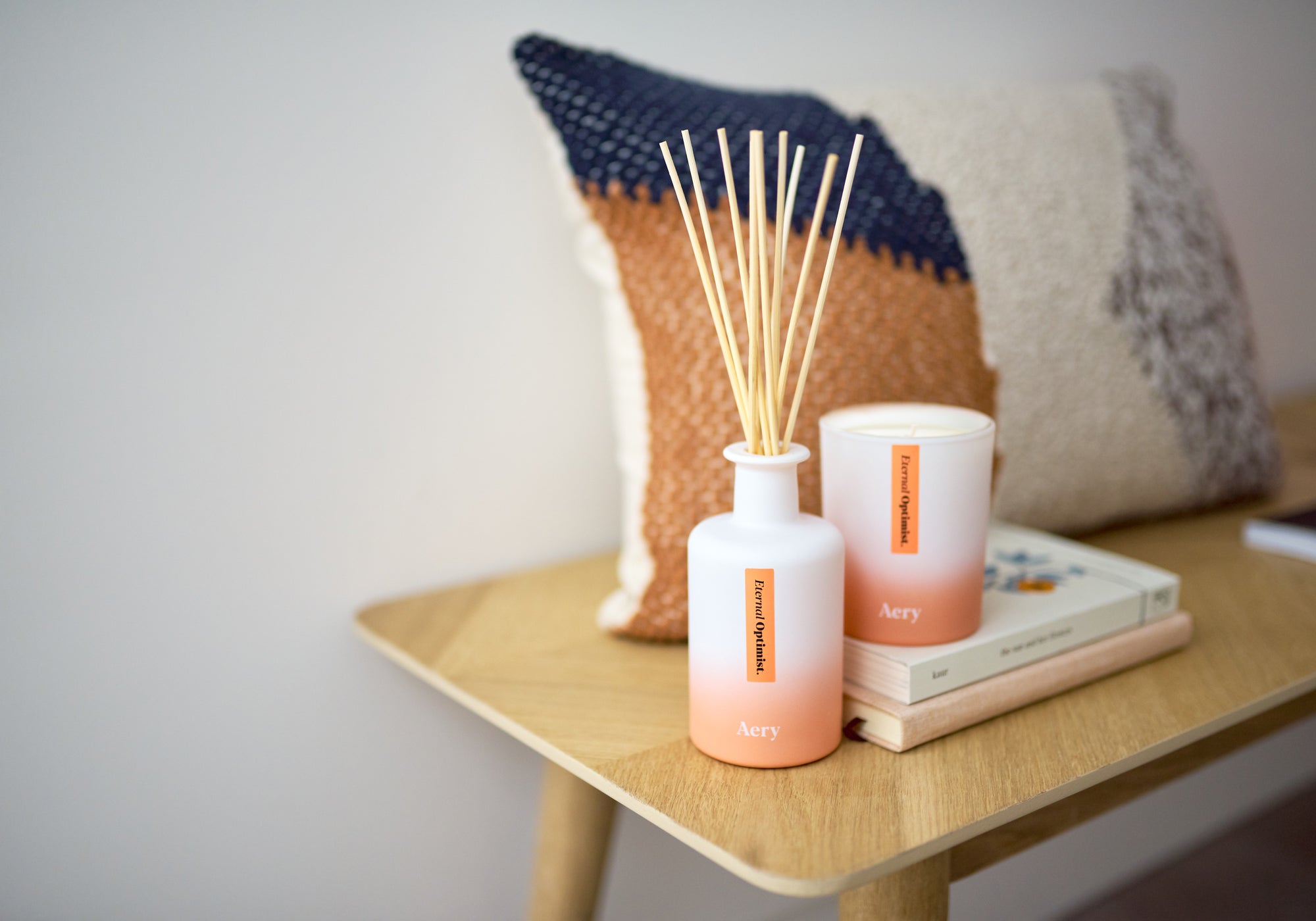 orange aery reed diffuser and matching candle displayed decoratively with cushion and books