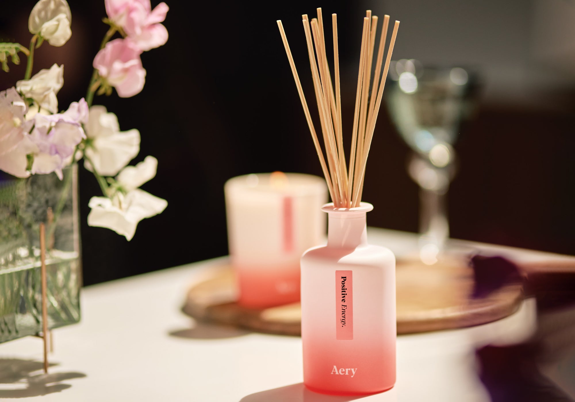 pink positive energy reed diffuser by aery living displayed in kitchen setting with matching candle in the background