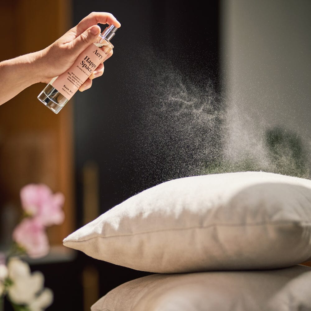 hand using happy space room mist on a stack of cushions