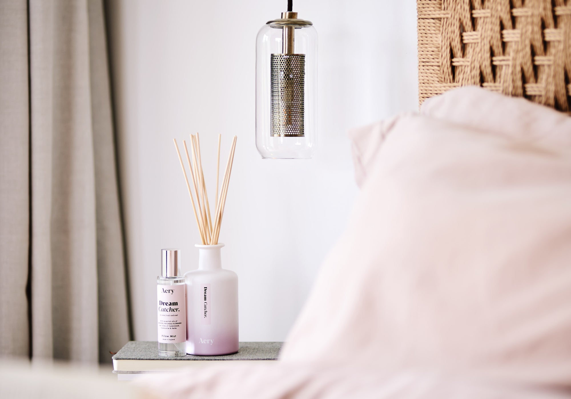 bedside setting with dream catcher reed diffuser displayed next to matching pillow spray with bedside lamp and pink bedding